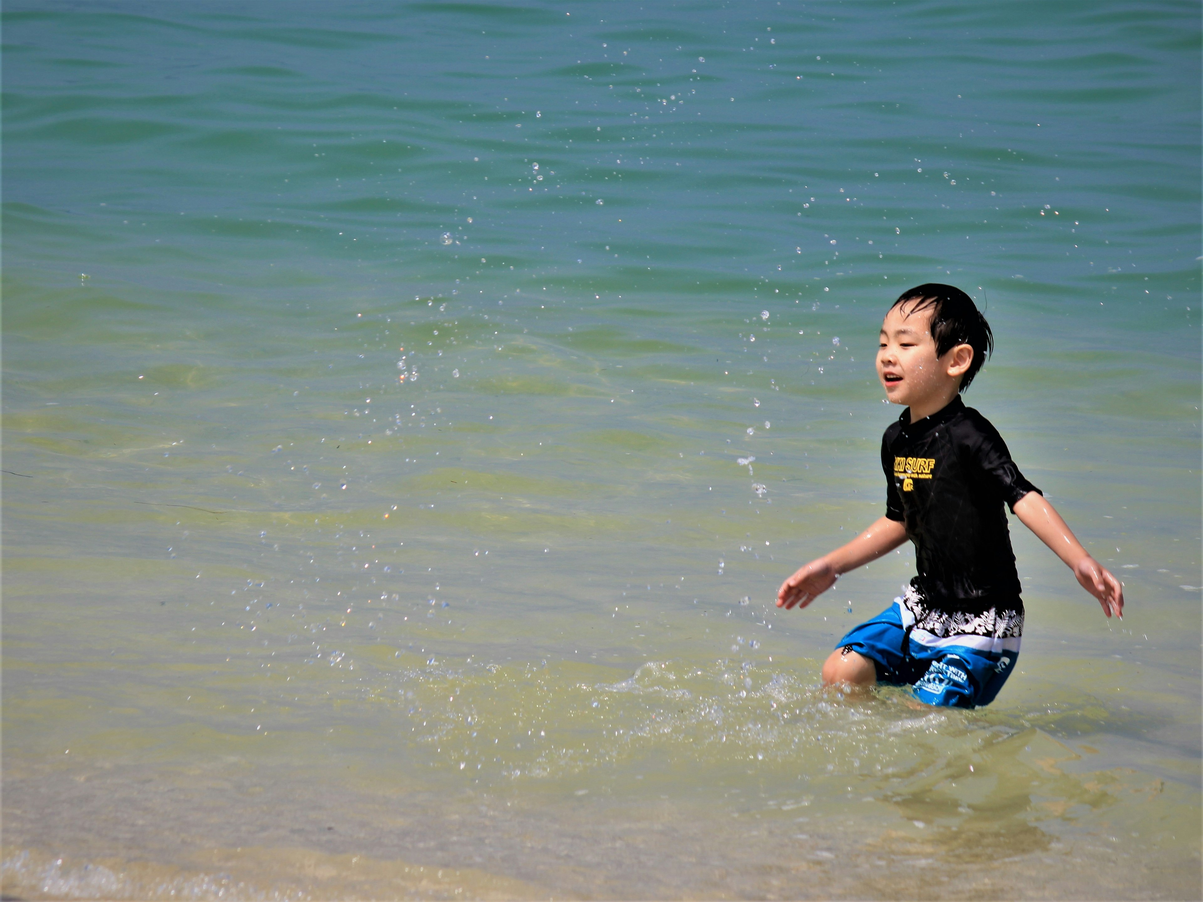 Bambino che gioca nel mare con schizzi d'acqua e un'espressione felice