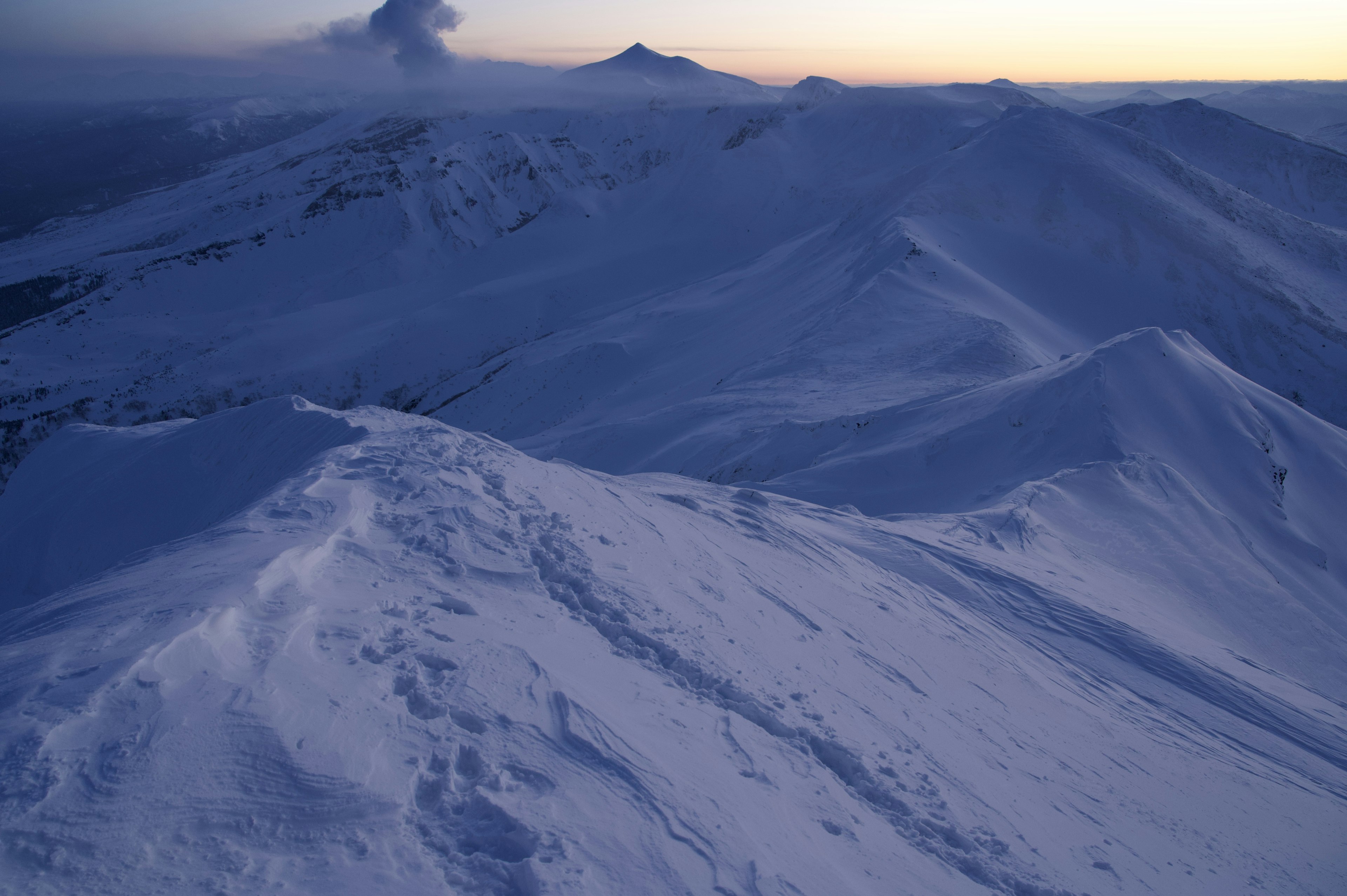 Snow-covered mountain range with a distant volcano