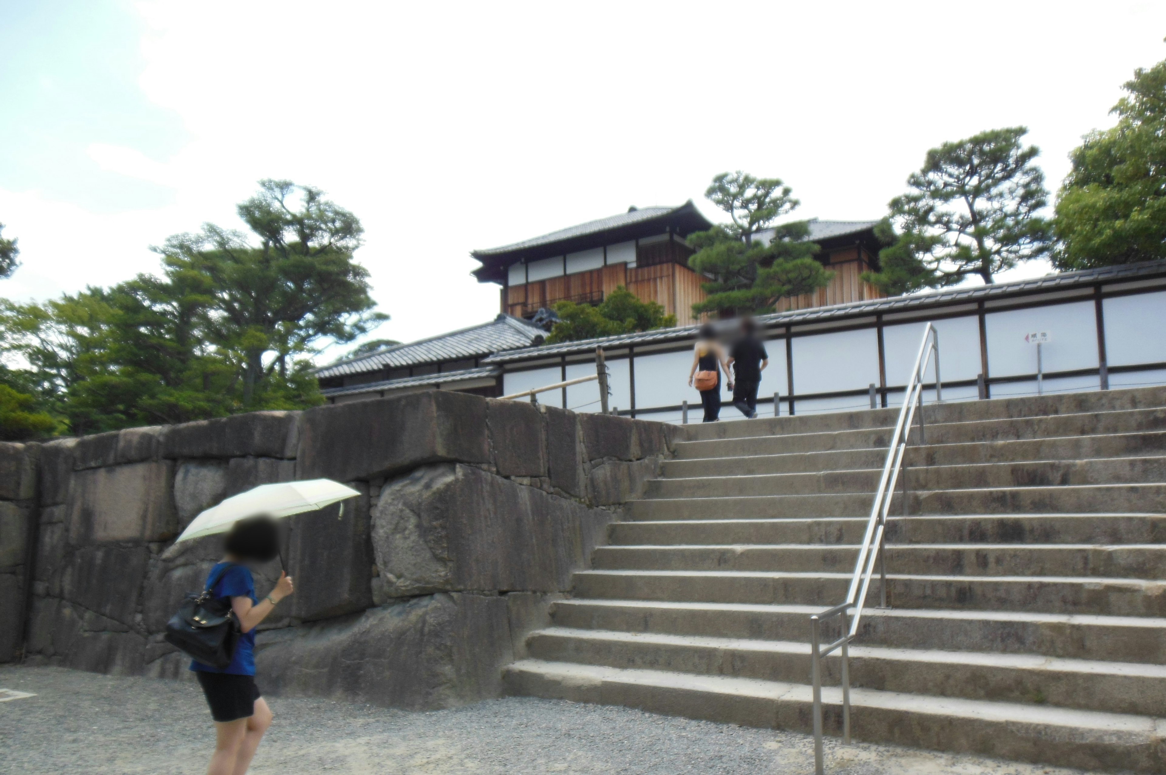 人們走上樓梯，遊客拿著雨傘 舊建築和綠色樹木可見