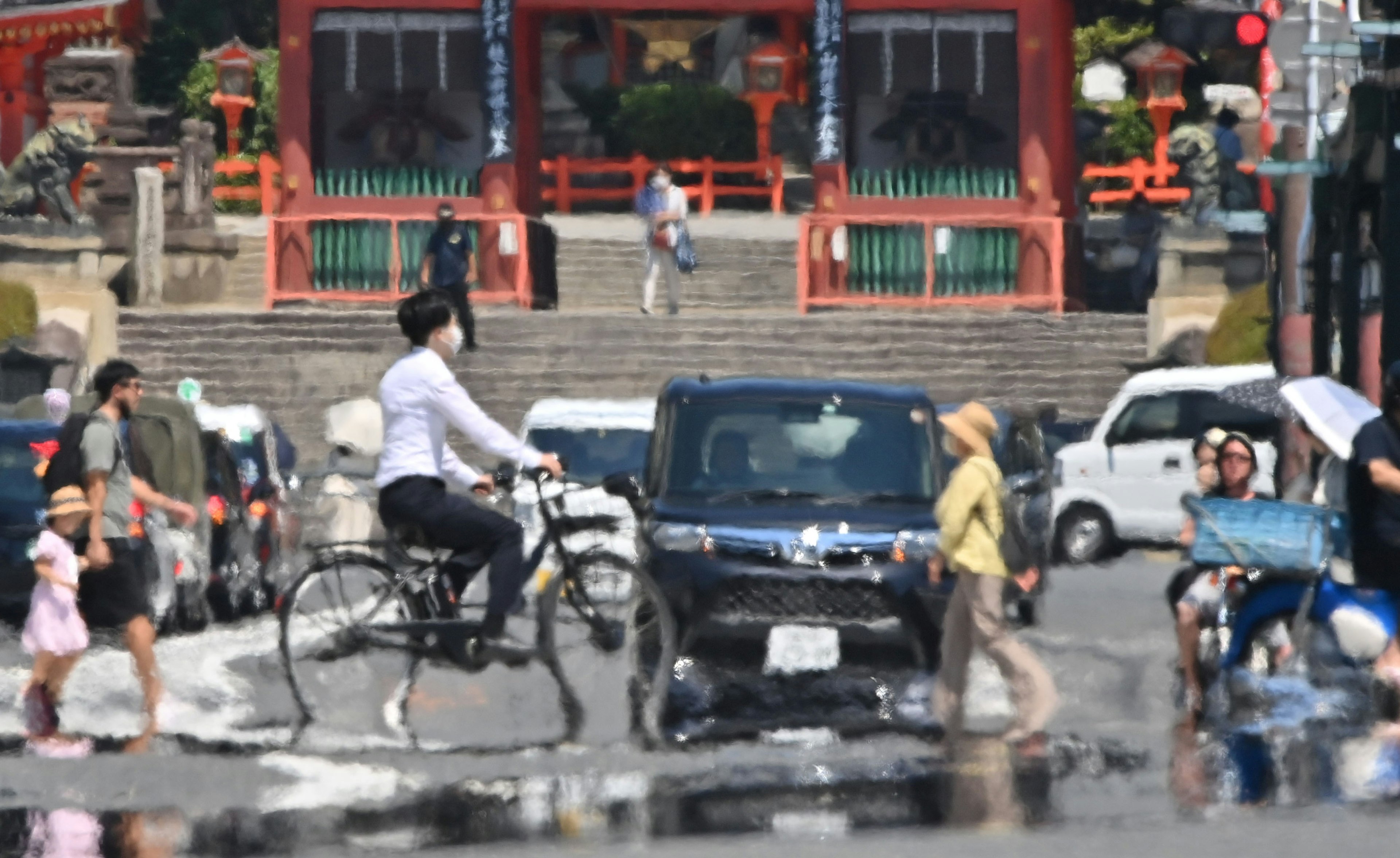 Una escena callejera concurrida con un hombre en bicicleta y un coche cruzándose con escaleras de templo y peatones