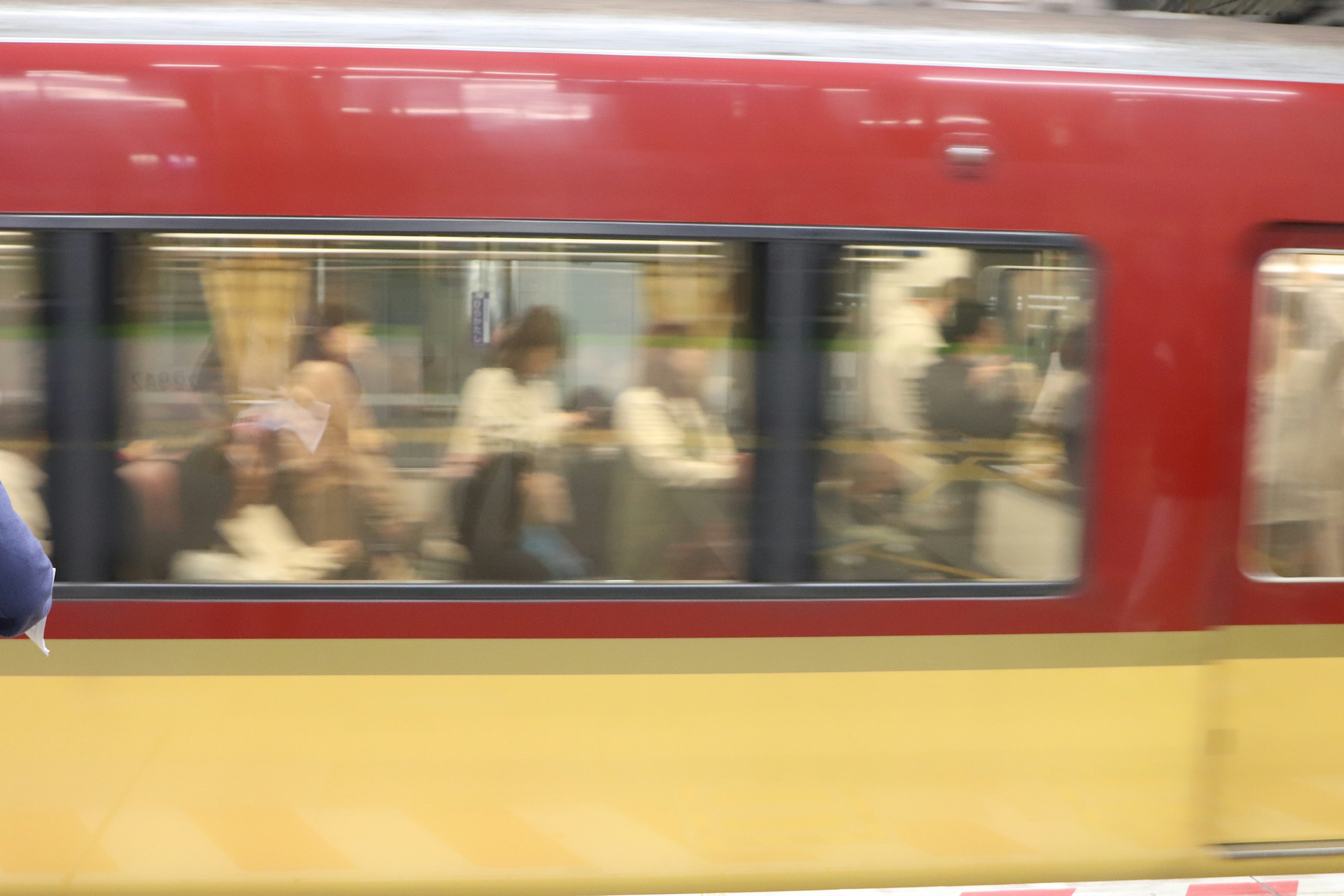 Train rouge et jaune passant par une gare avec des passagers visibles à travers les fenêtres