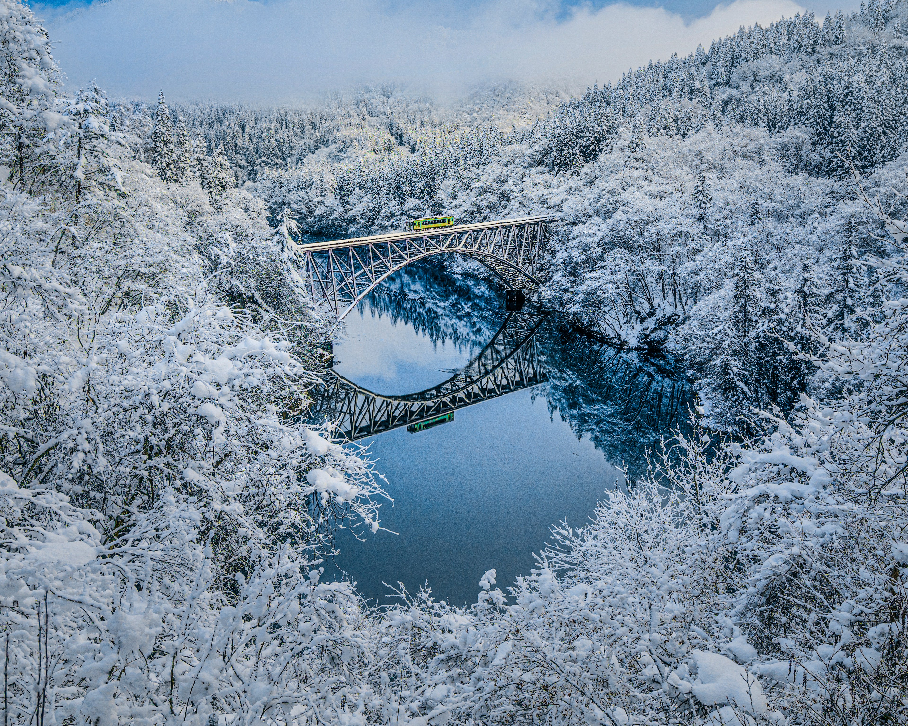 Ponte innevato che attraversa un lago tranquillo circondato da alberi invernali