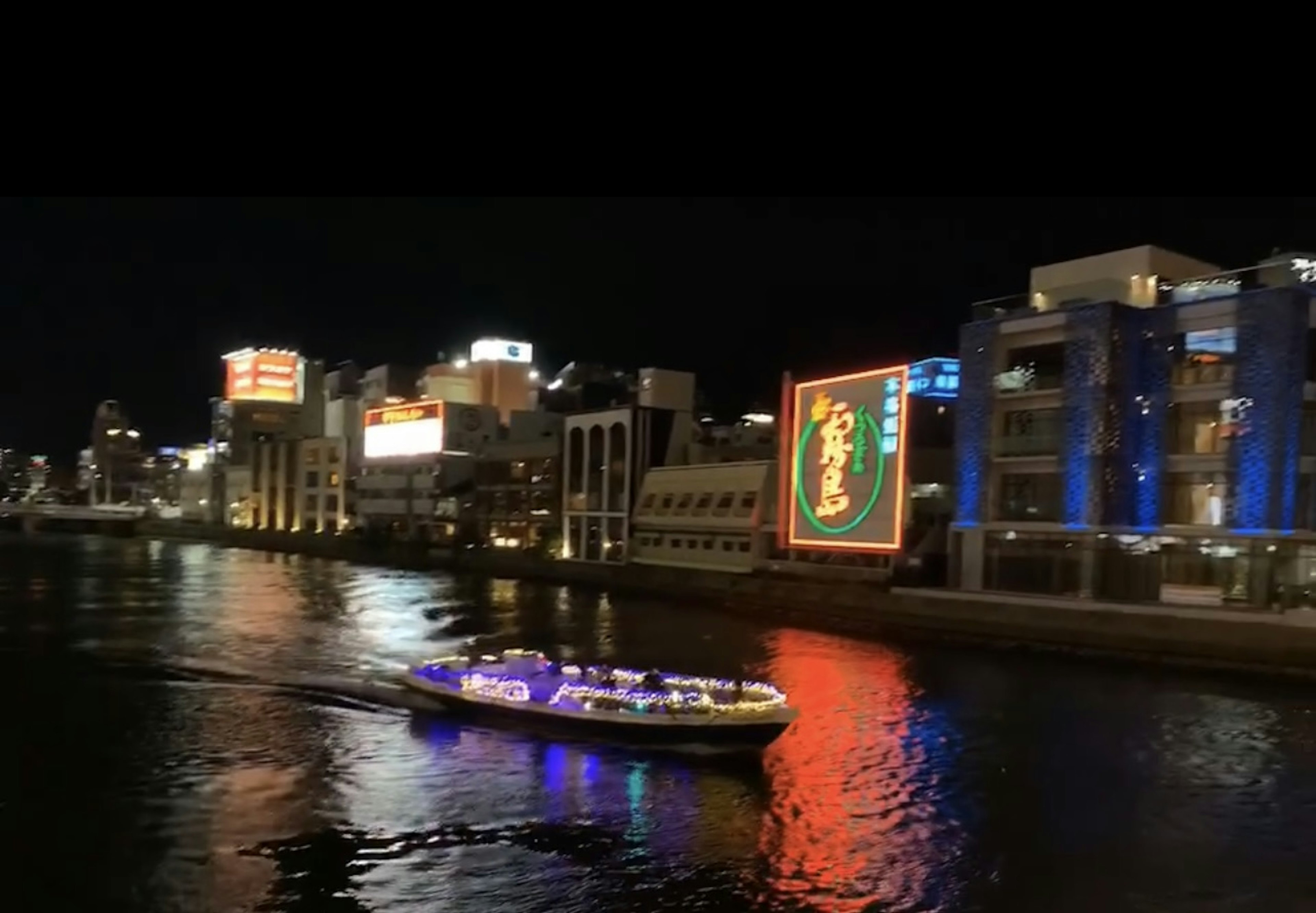 夜の川に浮かぶ観光船と明るいビルの景観