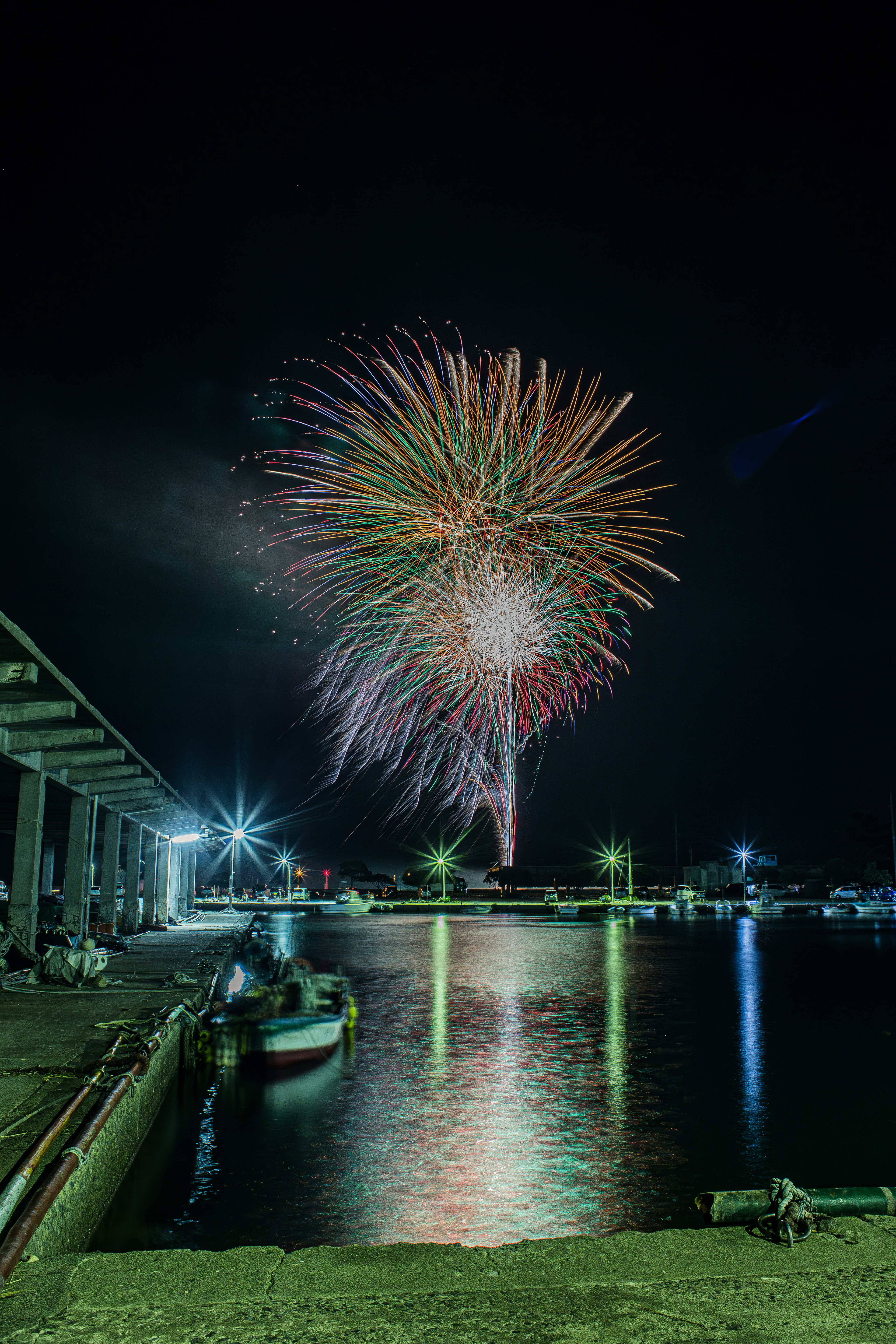 Colorful fireworks bursting in the night sky over a harbor reflecting on the water