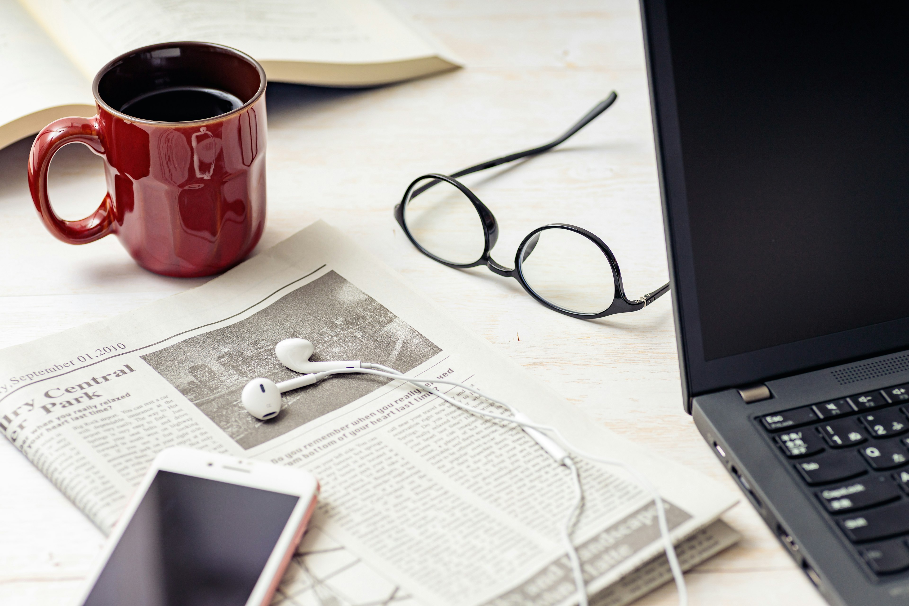 A red mug and newspaper on a desk with a laptop and smartphone