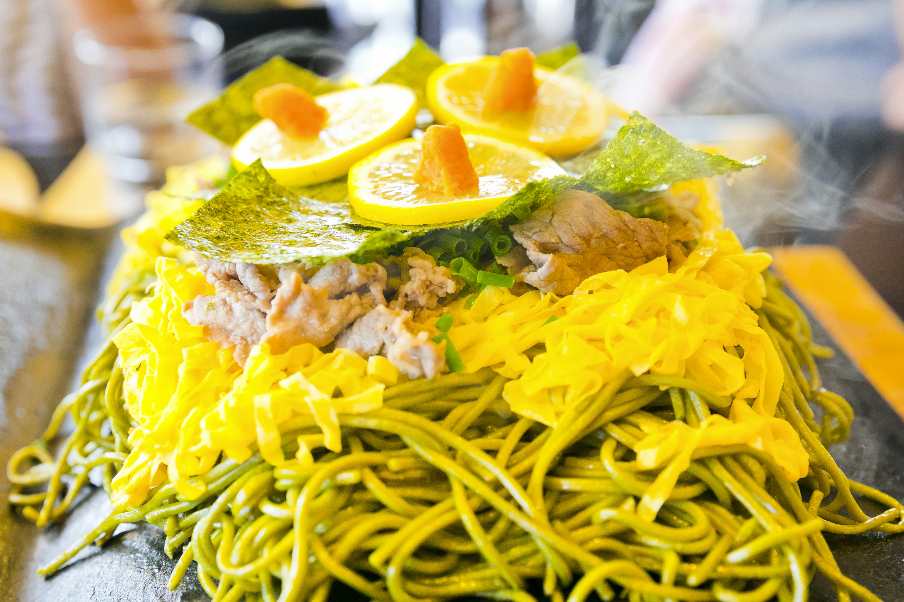 Plato con fideos verdes cubiertos con rodajas de limón y verduras