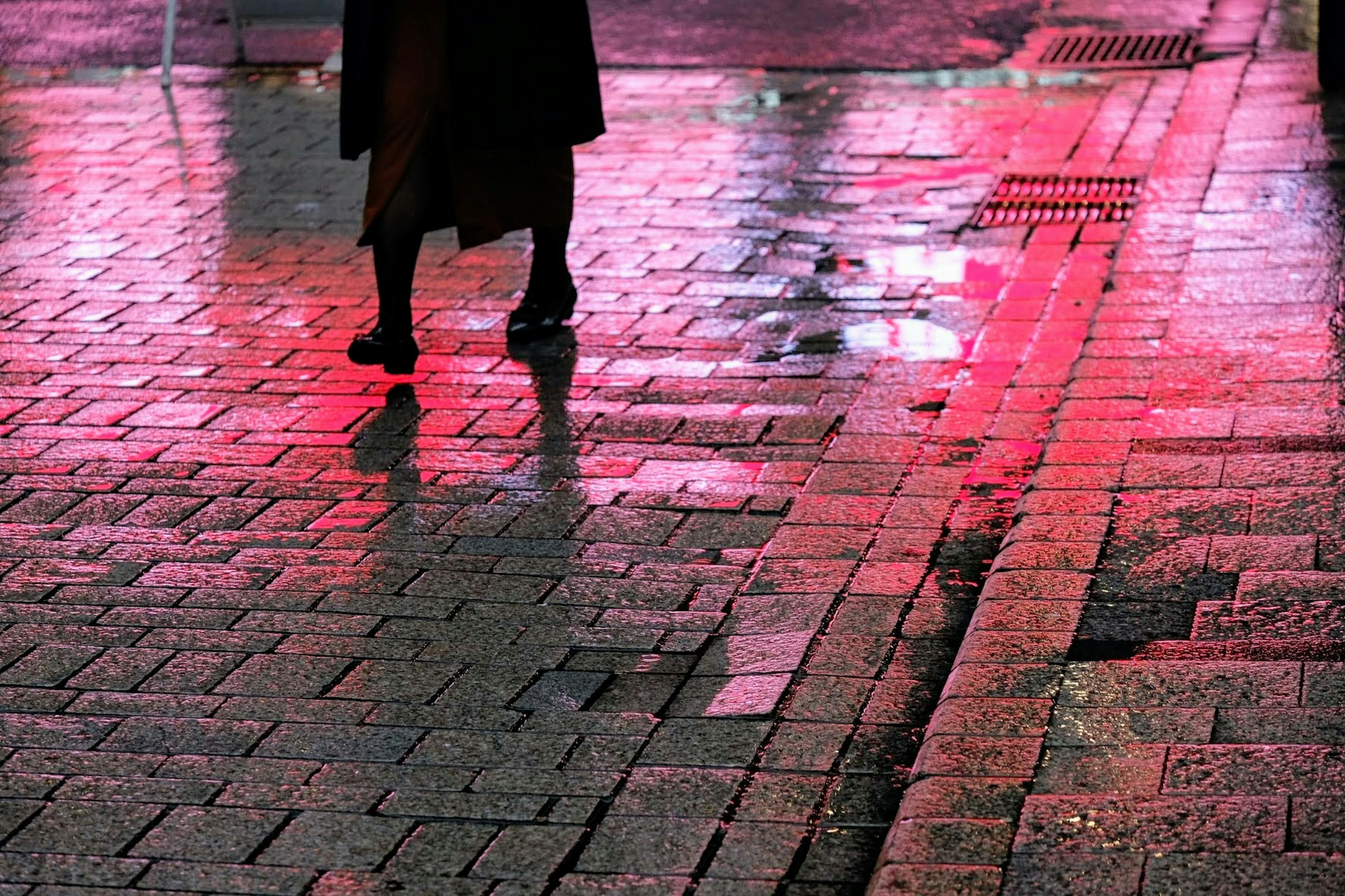 Silhouette of a person walking on wet cobblestones at night