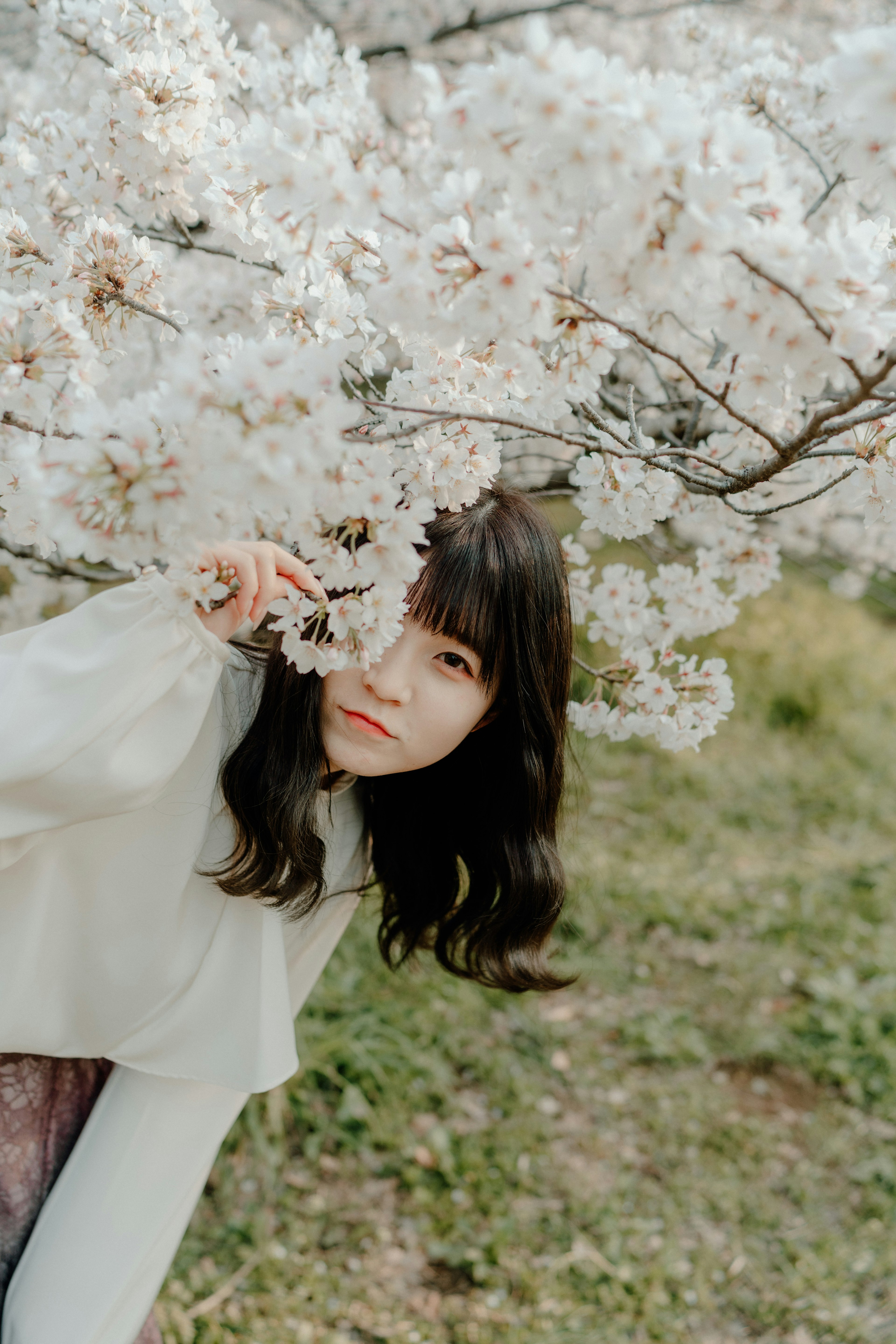 A woman smiling under a cherry blossom tree holding a flower