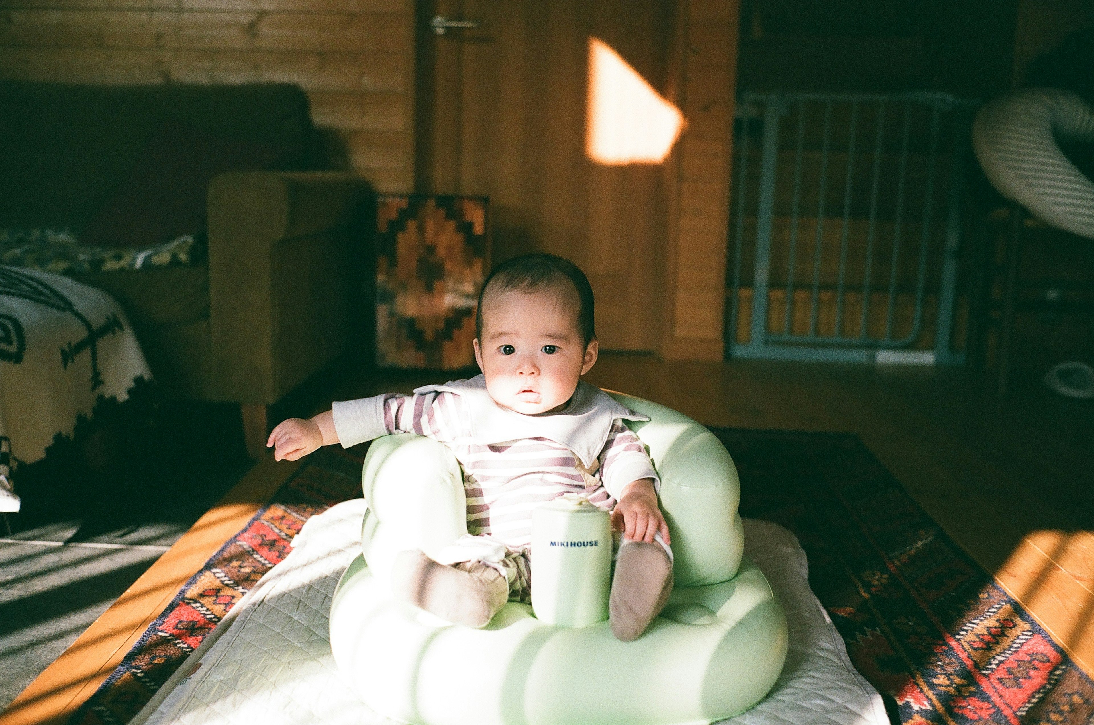 Baby sitting in a green support chair in a cozy indoor setting