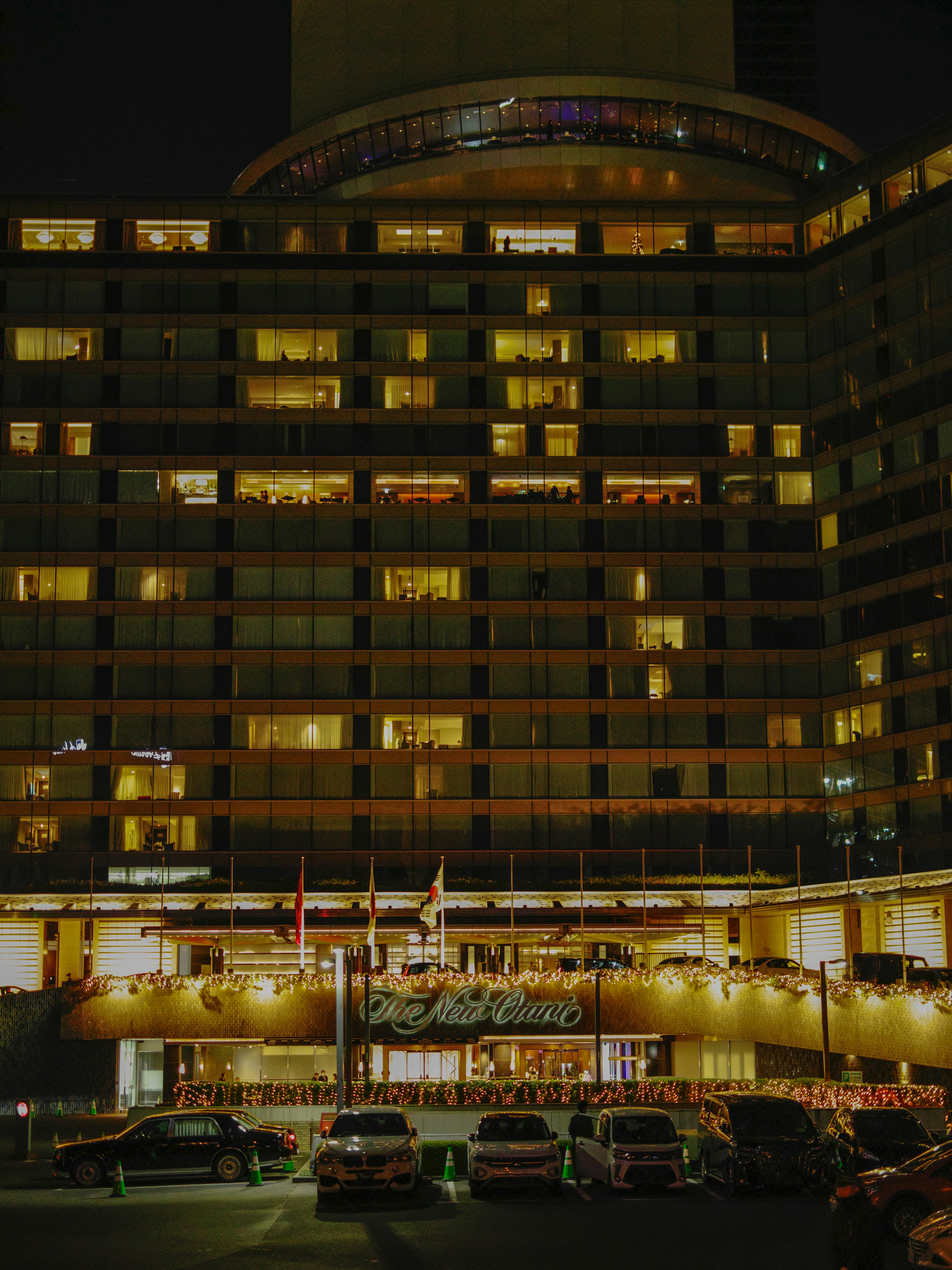 Vista nocturna de un hotel con ventanas iluminadas y coches estacionados