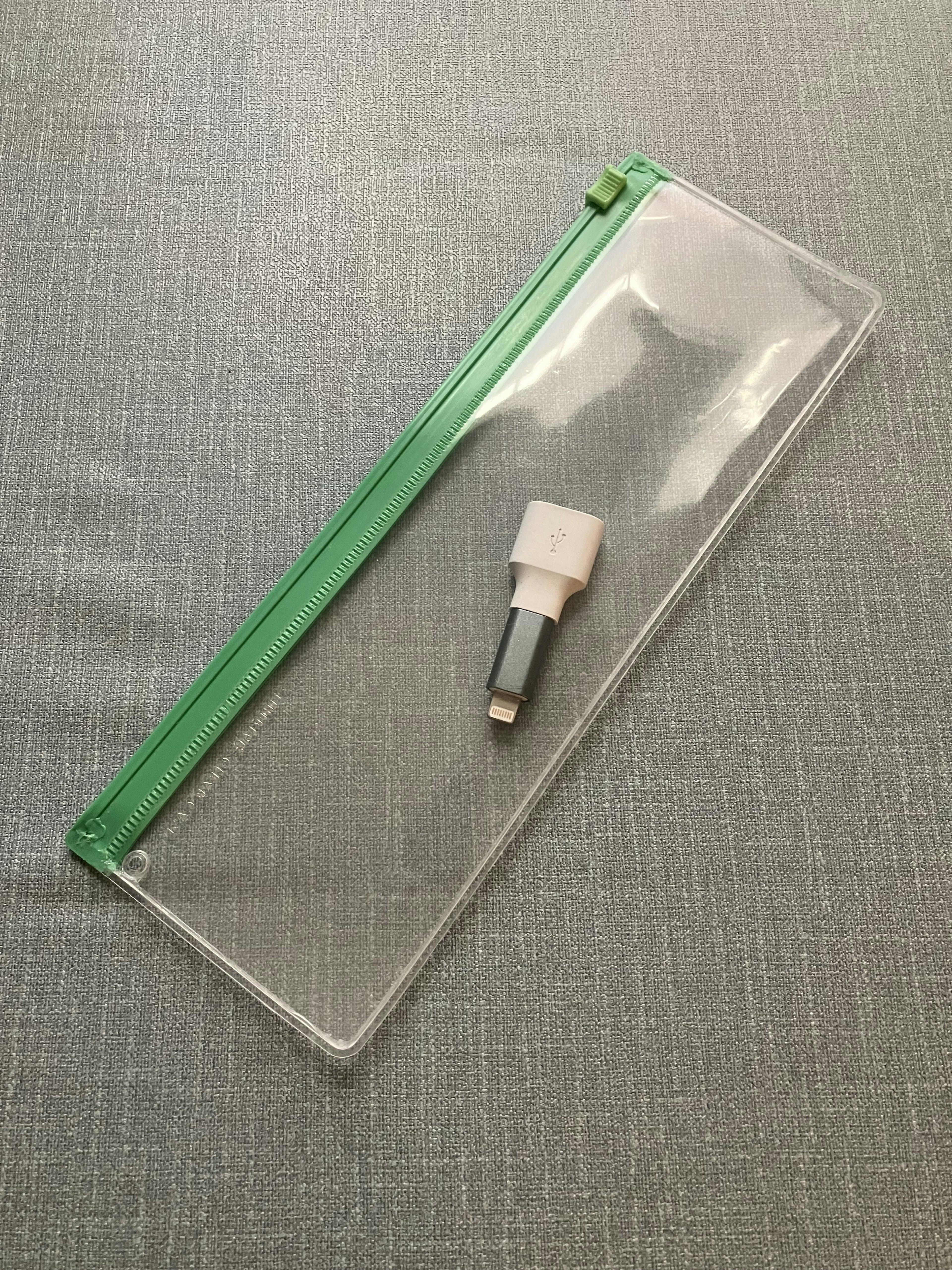 Transparent pouch with a green zipper and white pen