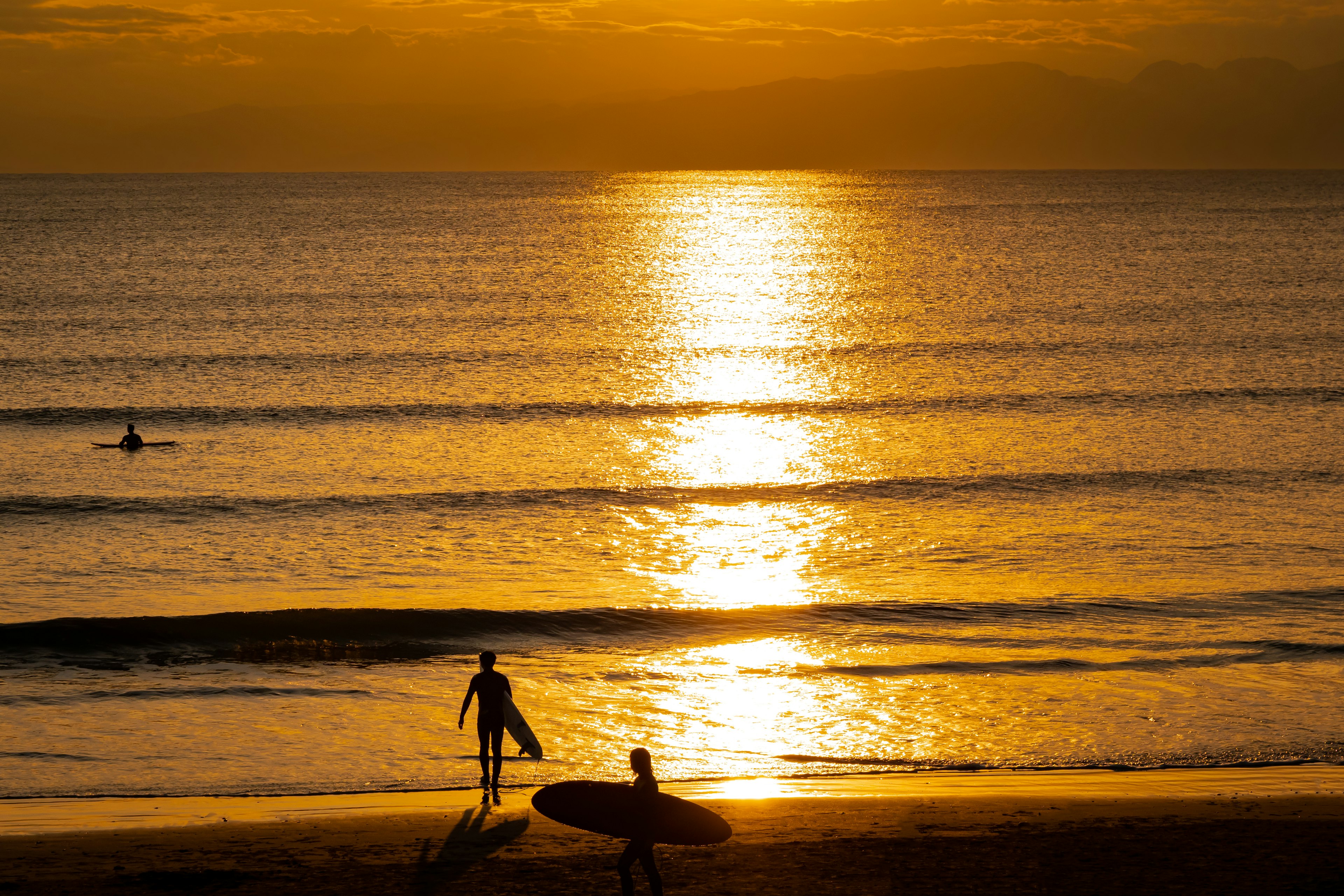 Silhouette di due surfisti con tavole da surf sulla spiaggia contro un tramonto