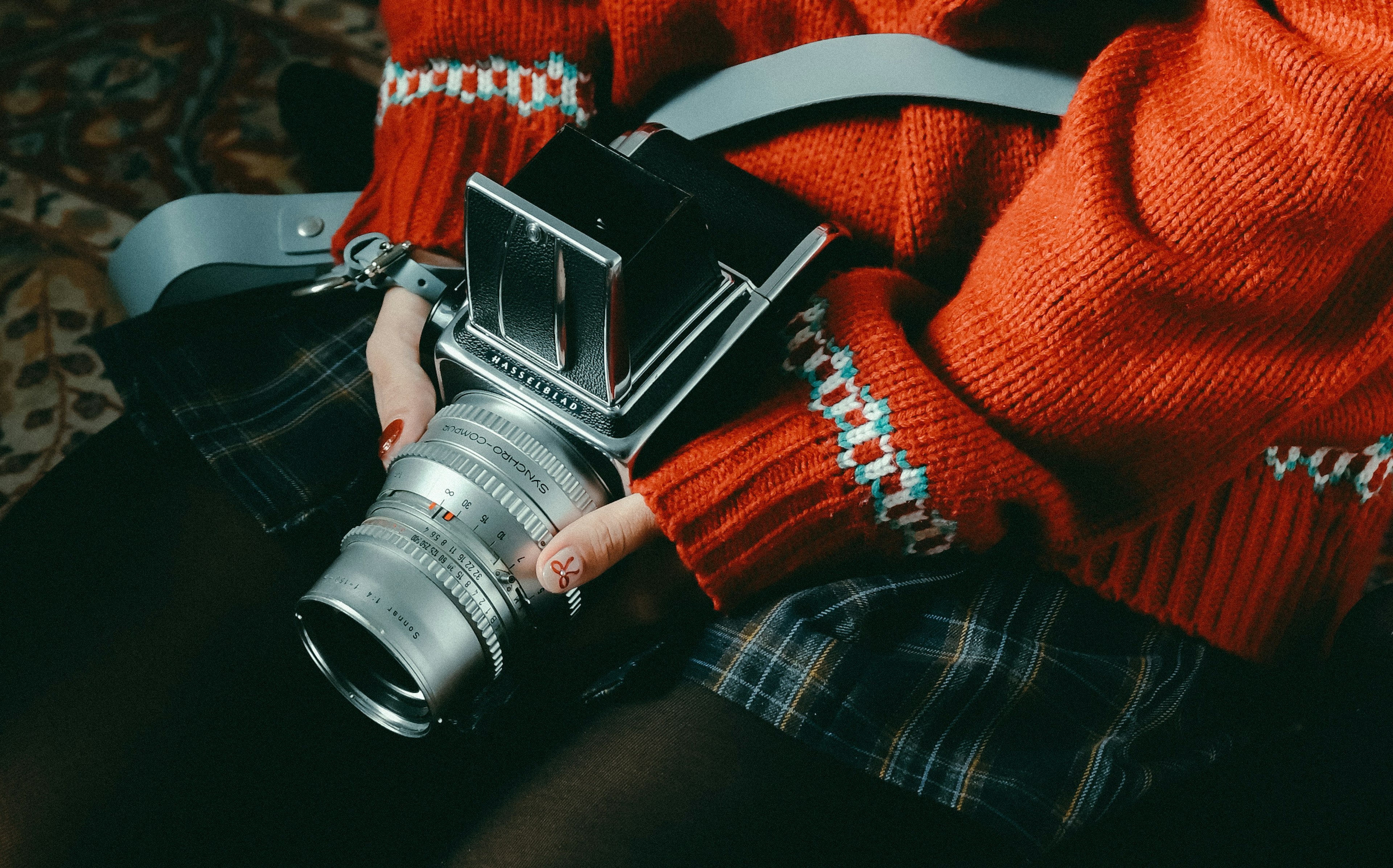 Persona con un maglione rosso che tiene una macchina fotografica argentata