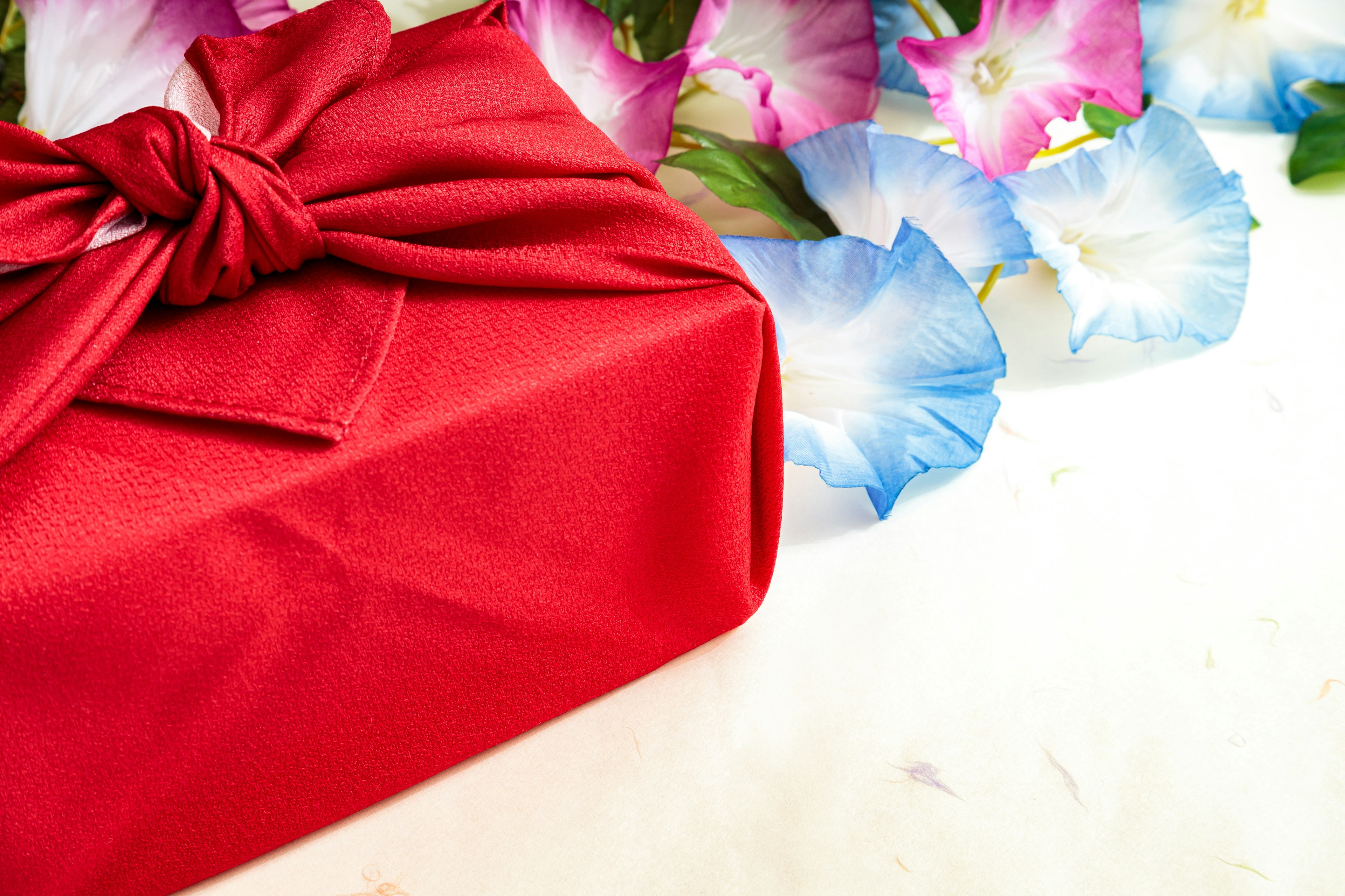 A red wrapped gift alongside colorful flowers