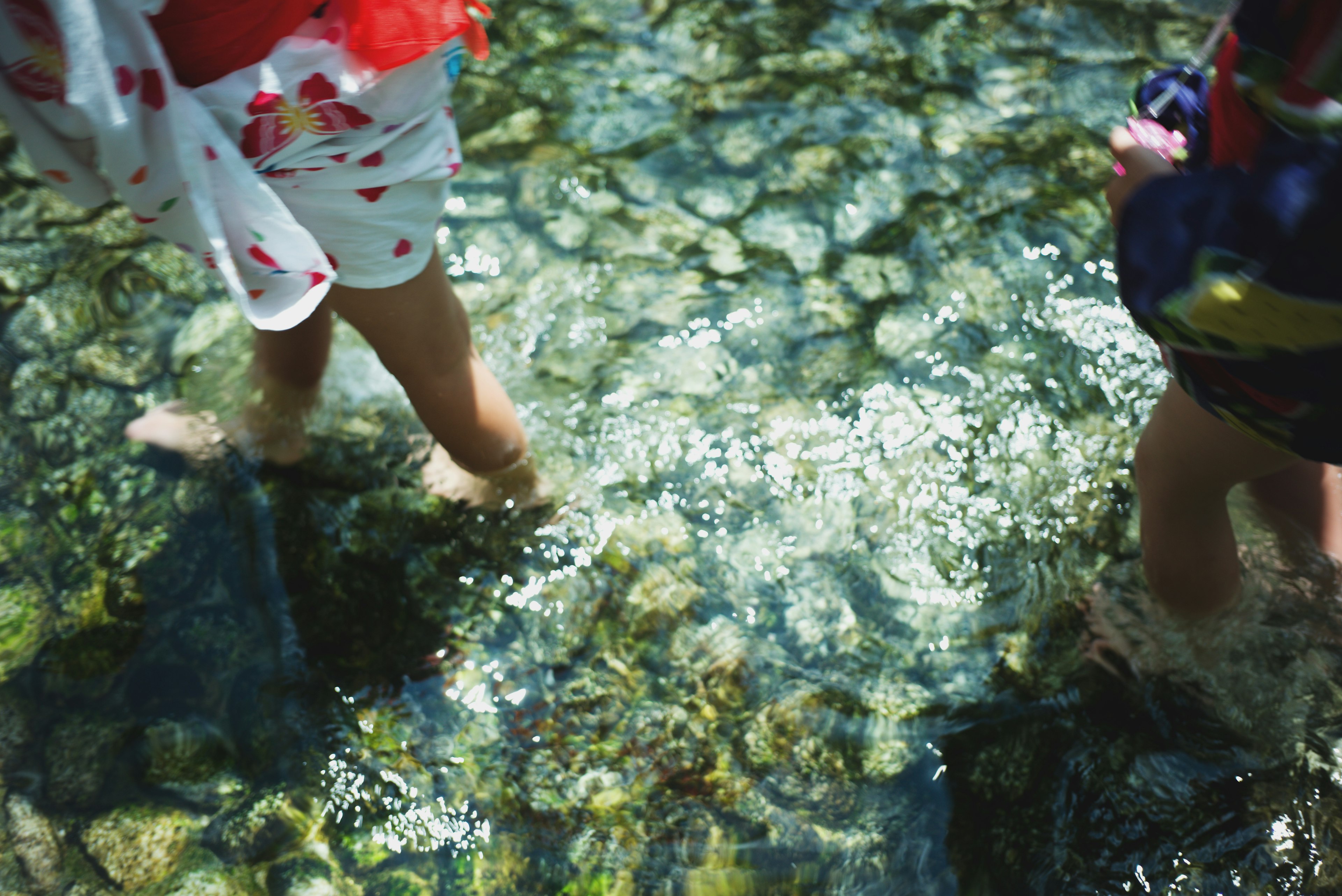 Bambini che camminano in acqua limpida con pietre visibili e riflessi di luce