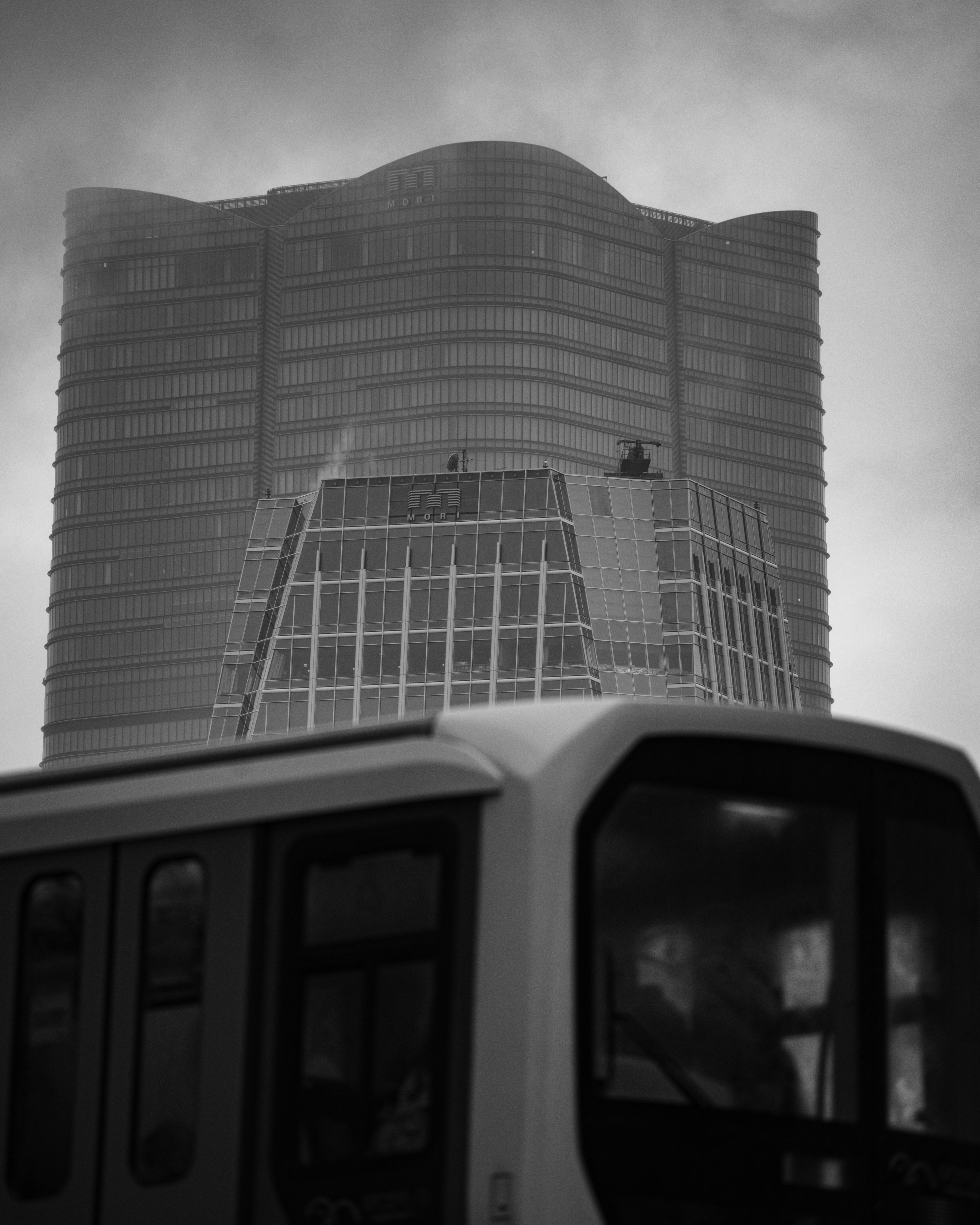 Paisaje urbano en blanco y negro con un rascacielos y parte de un vehículo de transporte