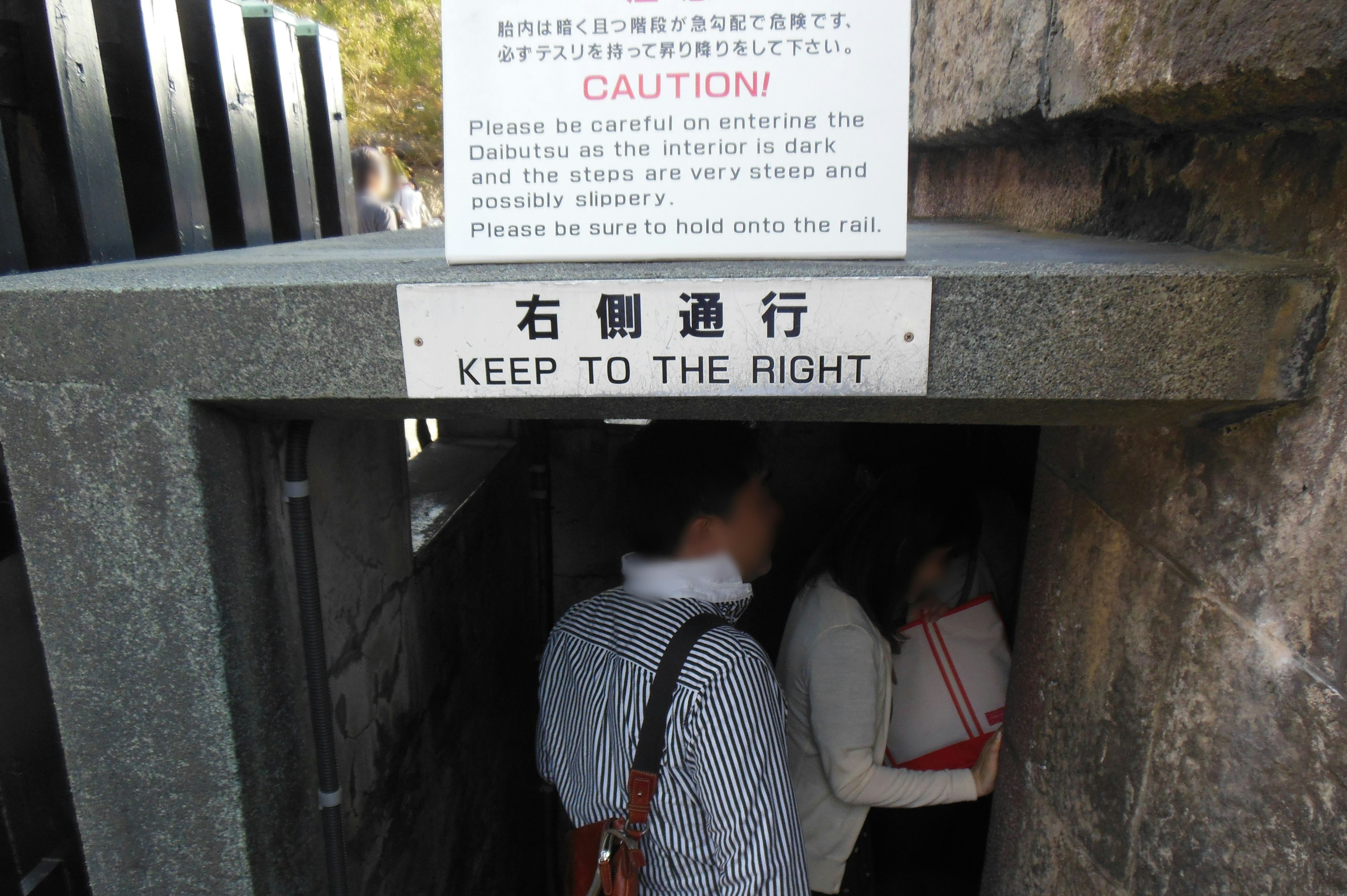 Entrance with warning sign and people passing through narrow passage