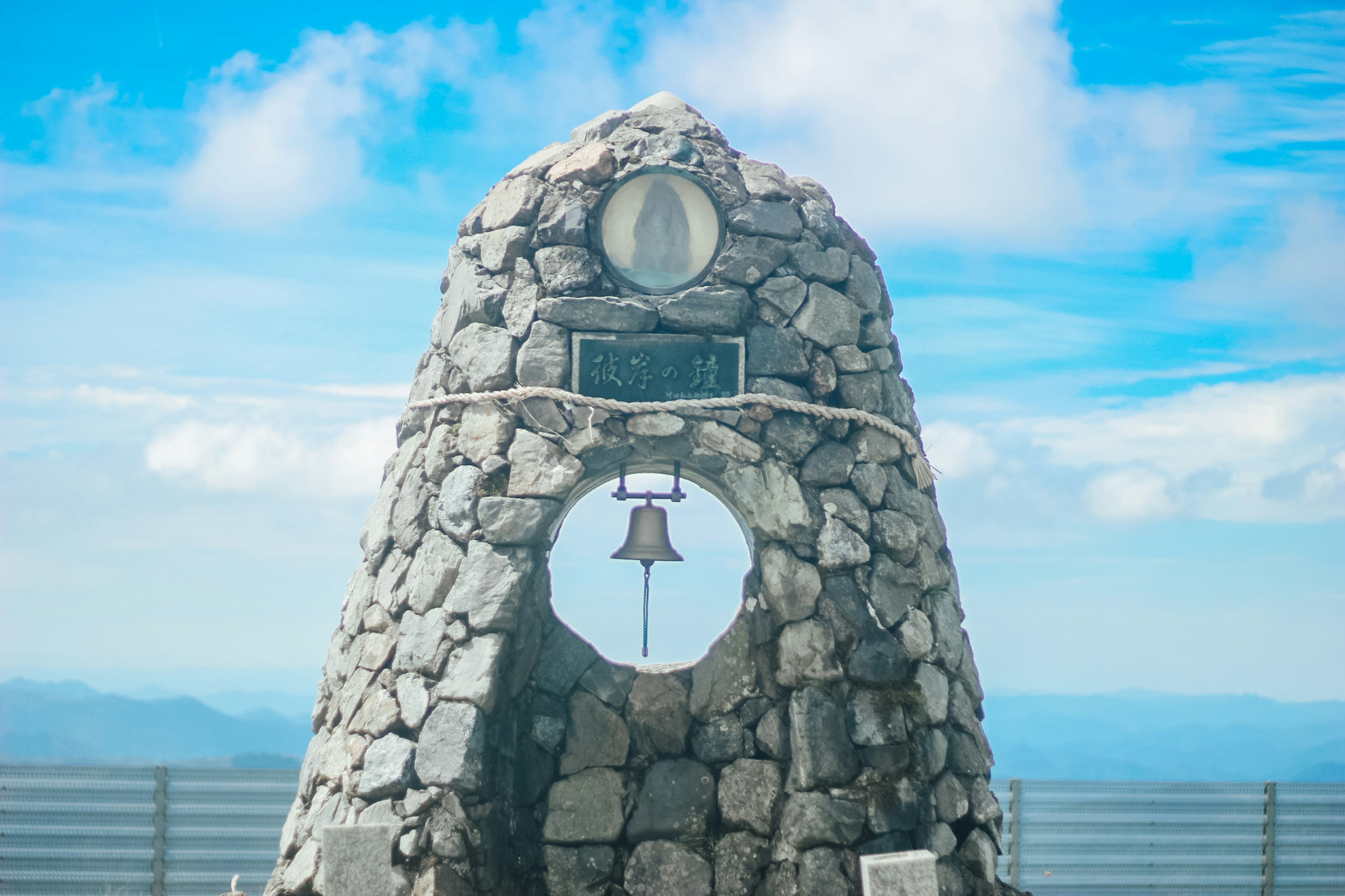 Monumen batu dengan lonceng di puncak gunung di bawah langit biru