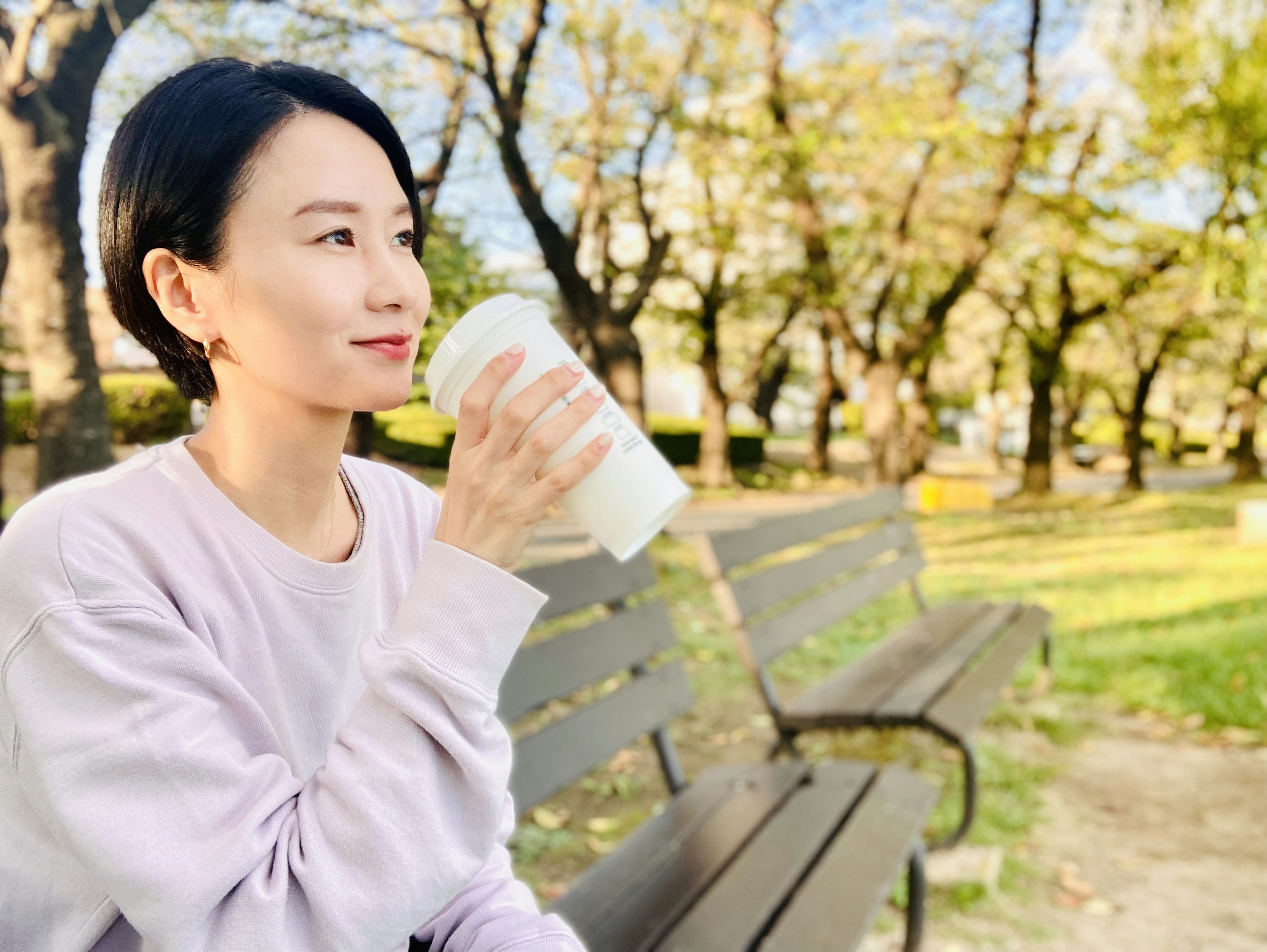 坐在公園長椅上，手拿飲料微笑的女性