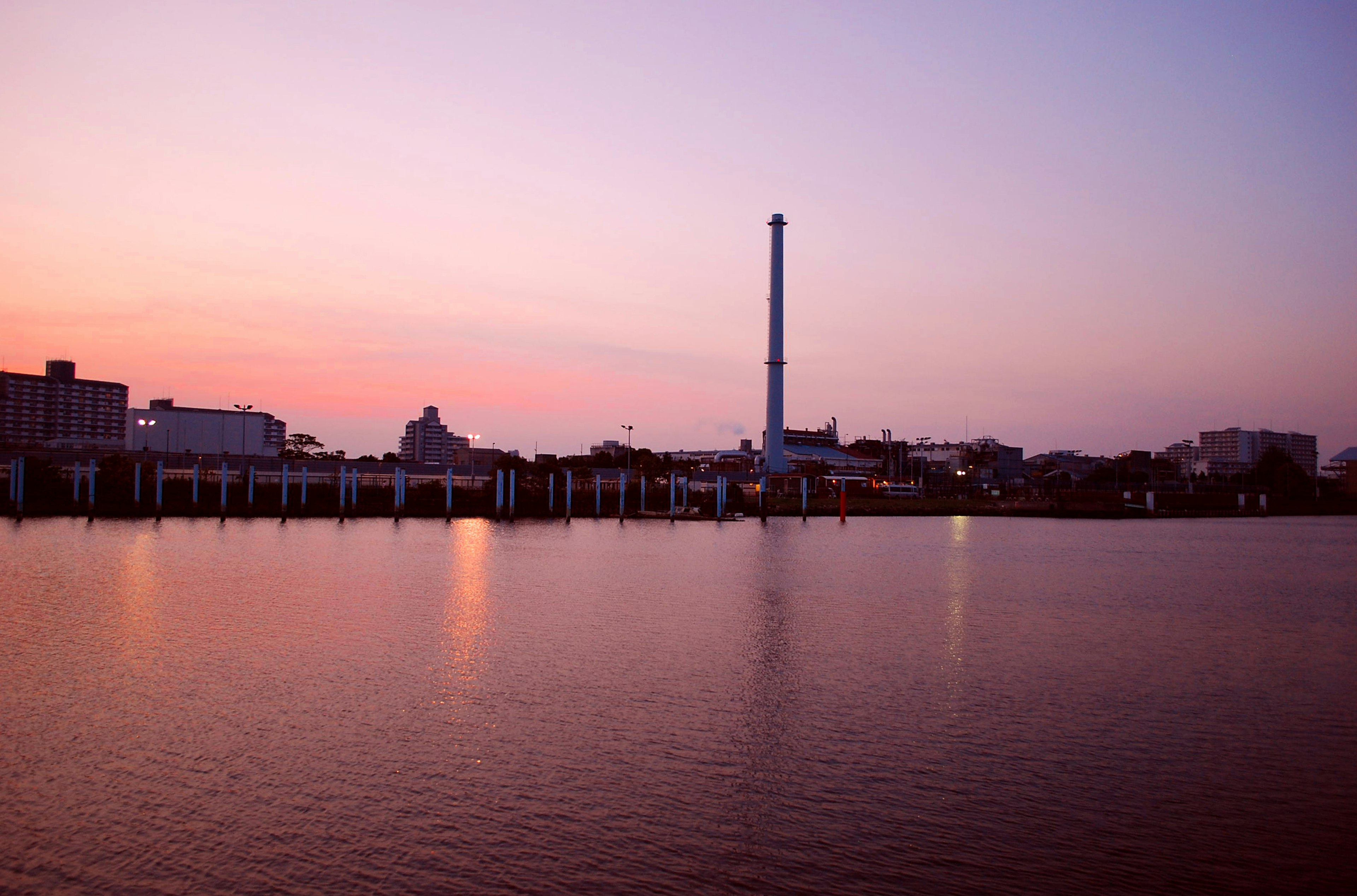 Fabrikschornstein und Gebäude, die sich im Wasser bei Sonnenuntergang spiegeln