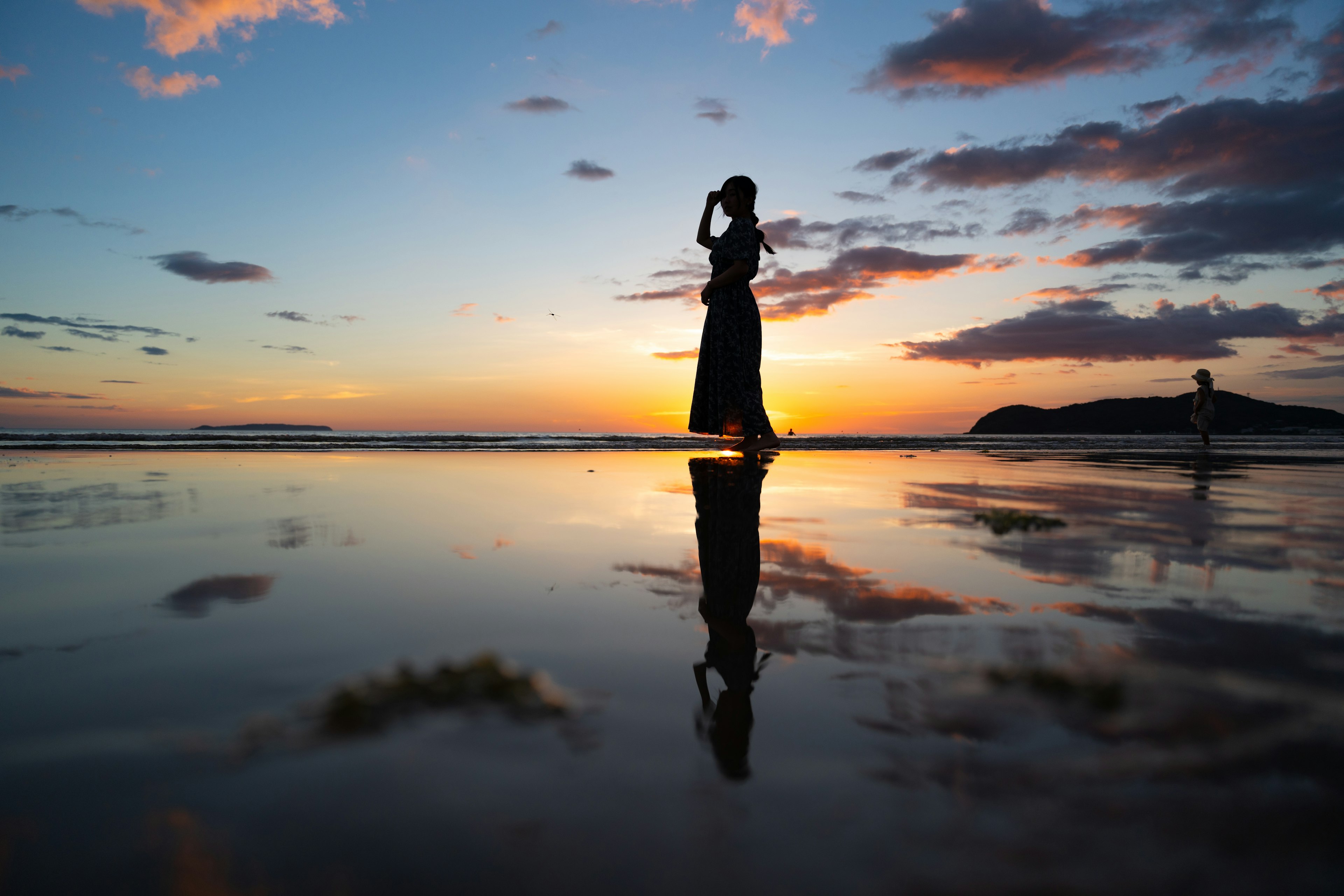 Silhouette einer Frau, die am Strand bei Sonnenuntergang steht mit Reflexionen im Wasser