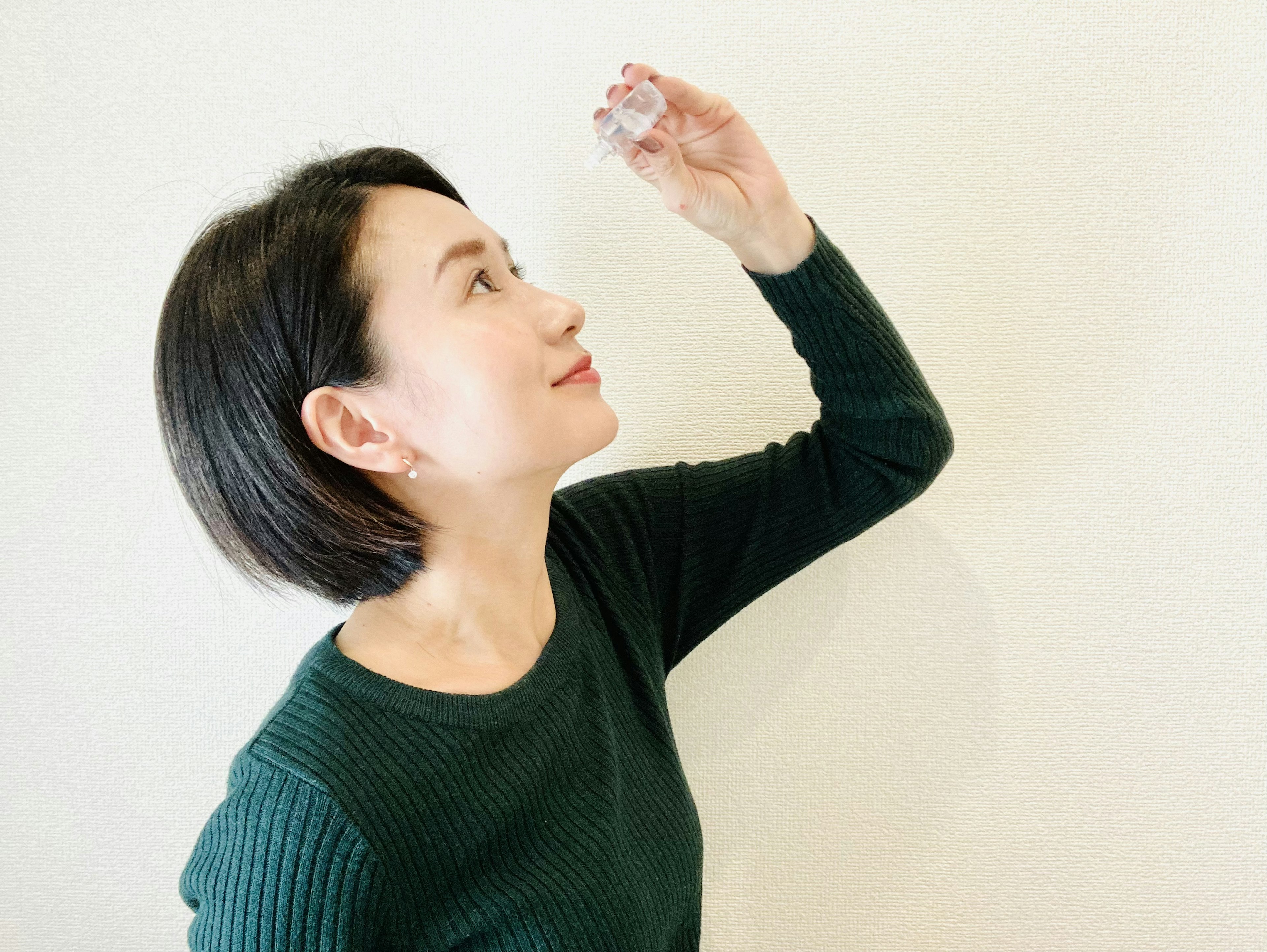 A woman holding a small object towards a white wall