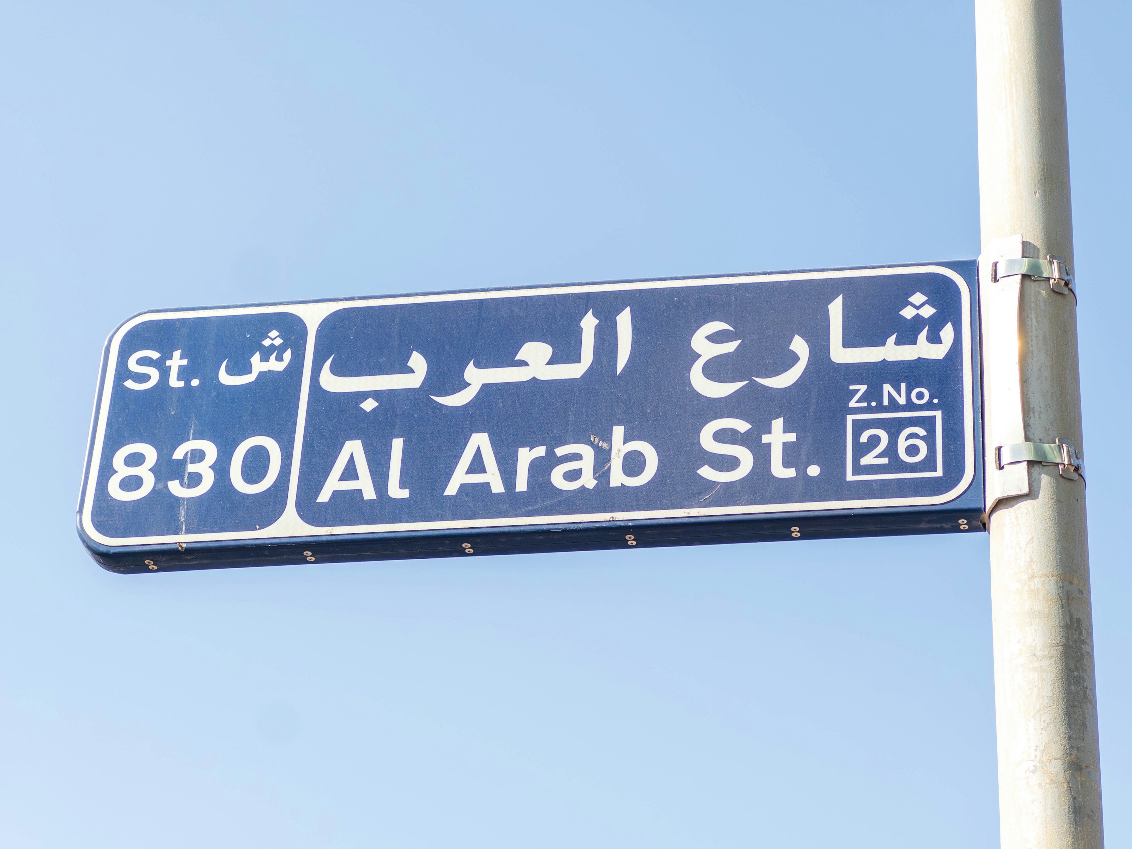 Señal de calle azul bajo un cielo despejado que muestra Al Arab St 830 en árabe e inglés