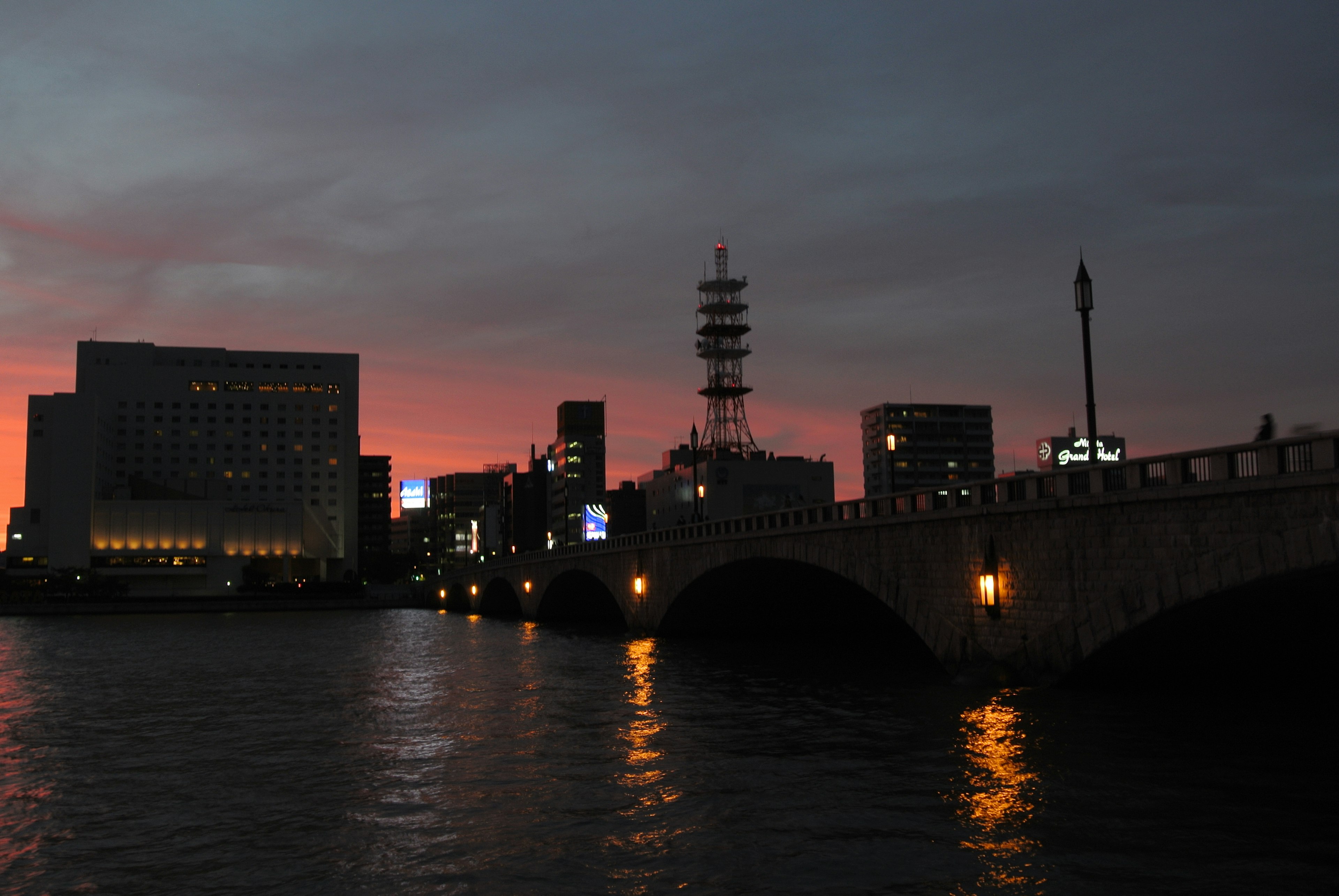 Silhouette de la ciudad al atardecer con un puente y reflejos en el agua