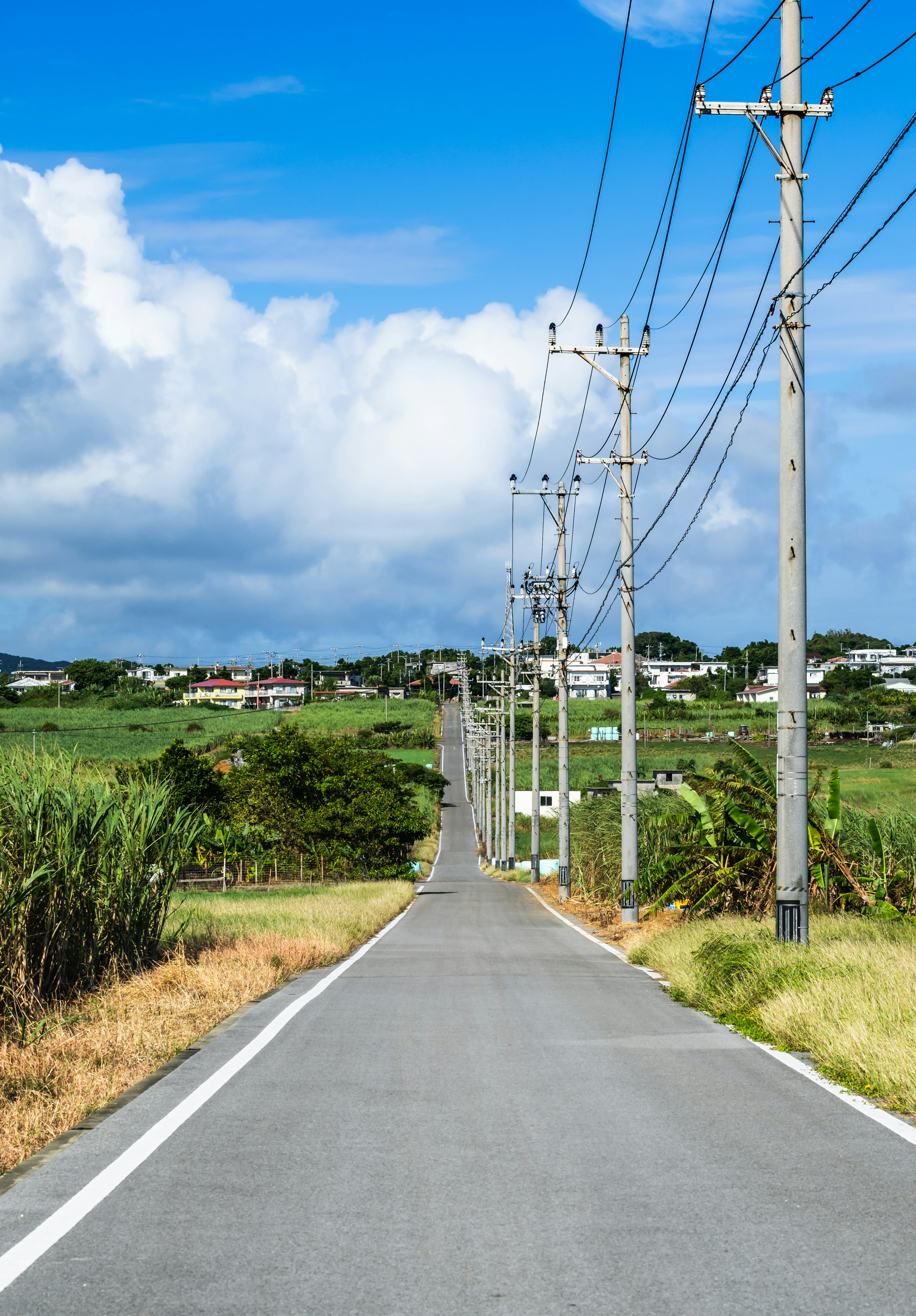 Lange Straße mit Stromleitungen unter einem blauen Himmel und weißen Wolken