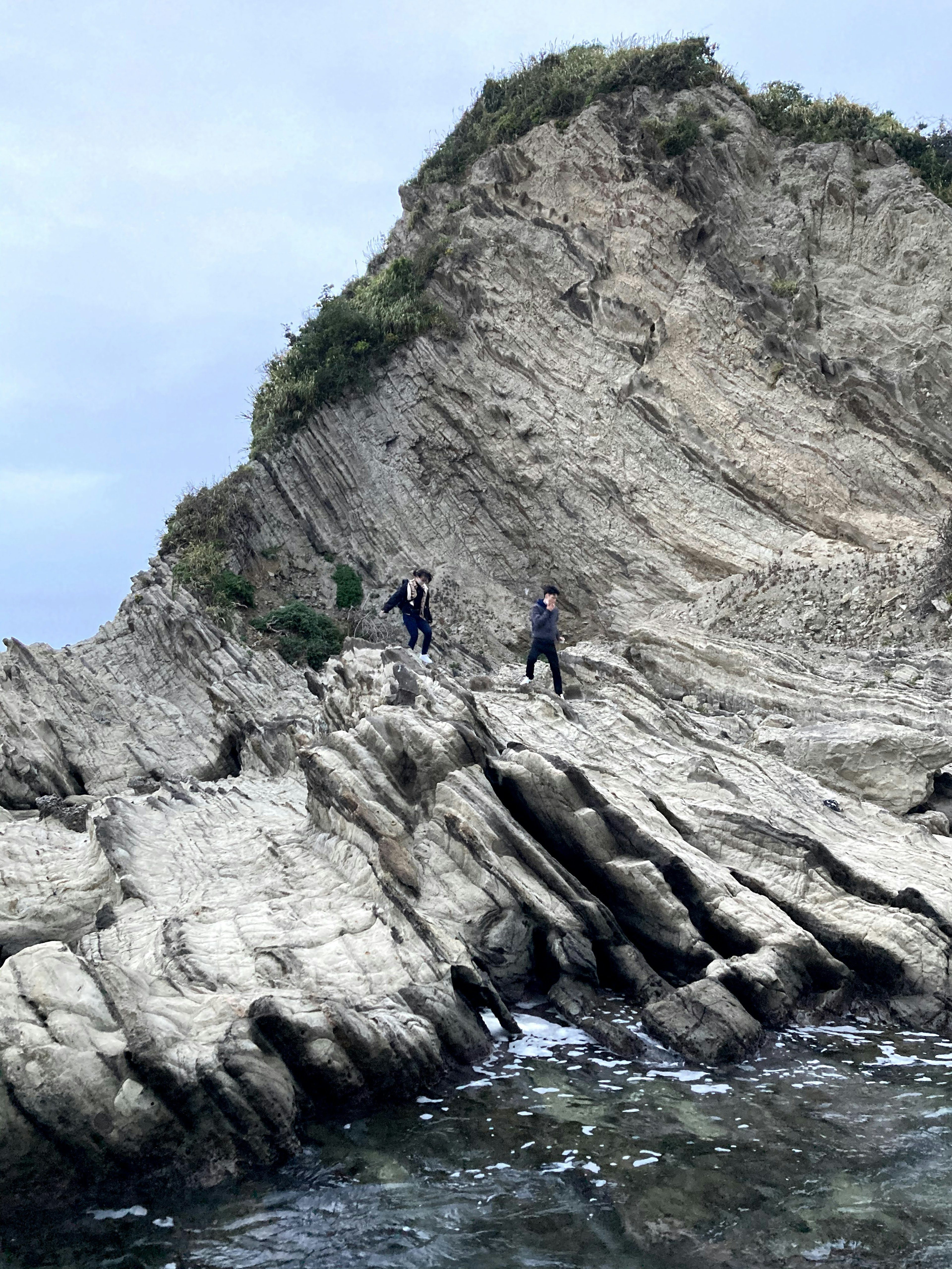 Dos excursionistas en una formación rocosa costera con características geológicas únicas