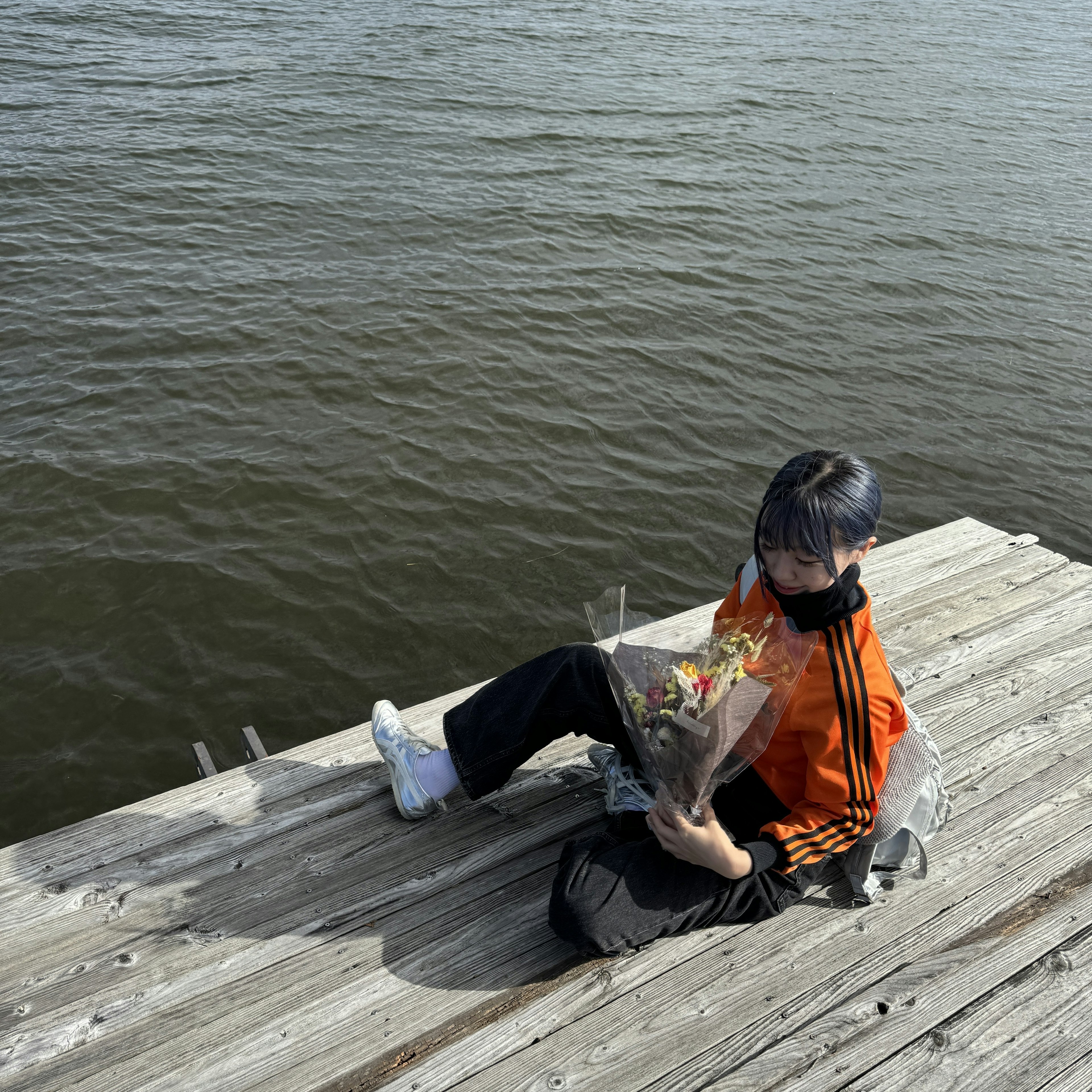 A boy wearing an orange shirt sitting by the water