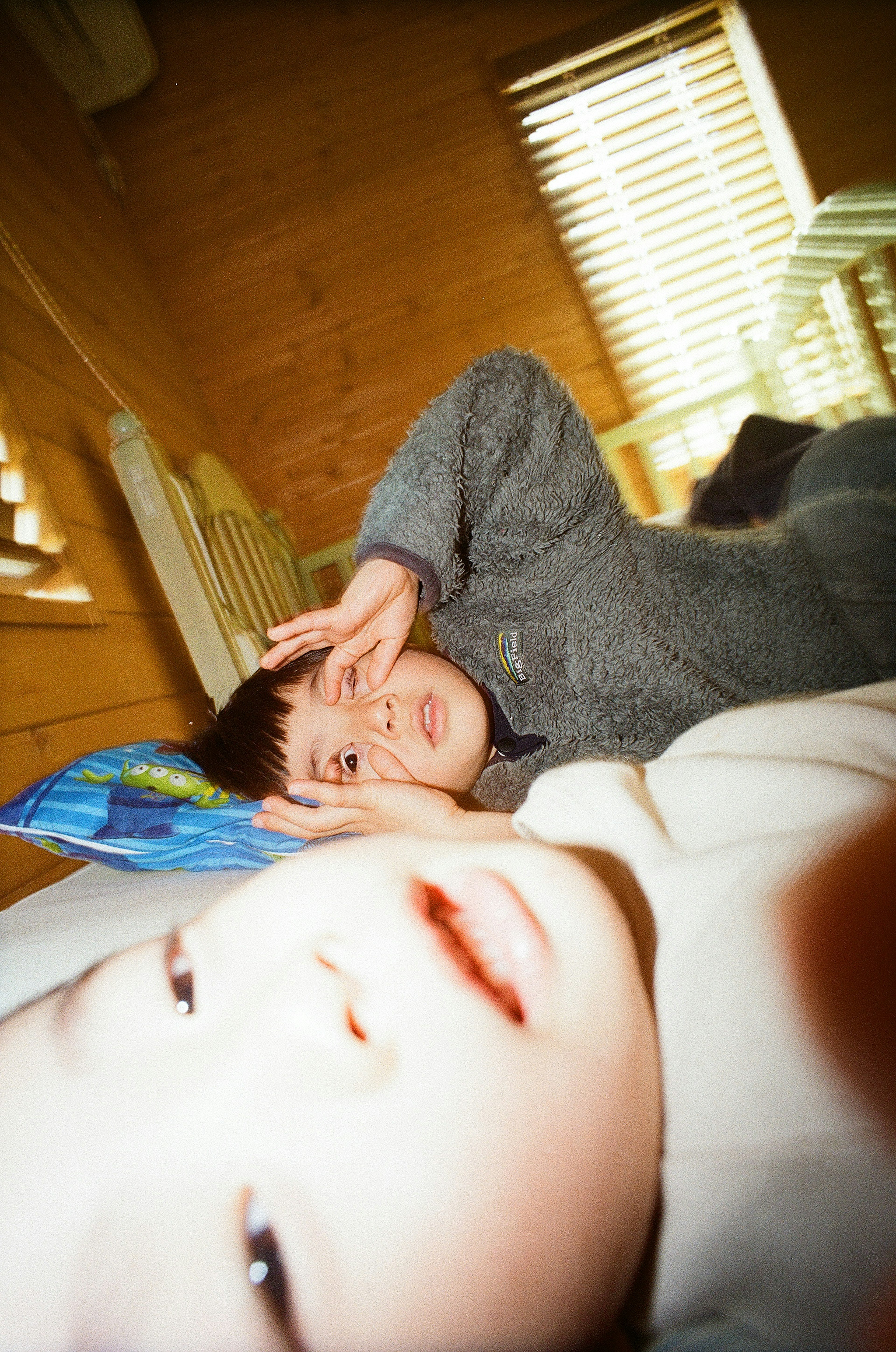 Dos niños acostados en una cama uno haciendo un signo de paz hacia la cámara