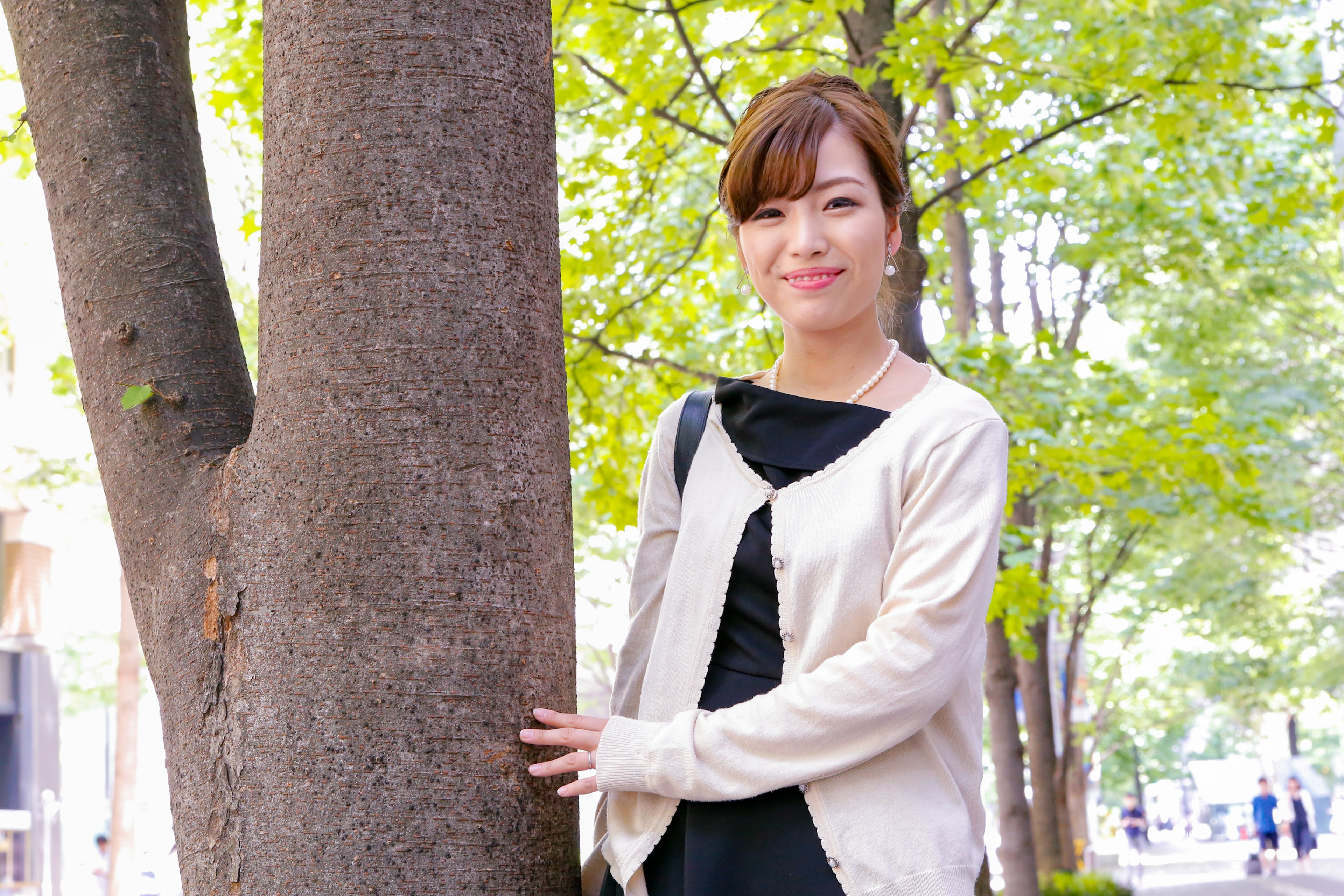 A woman smiling while leaning against a tree with a green background