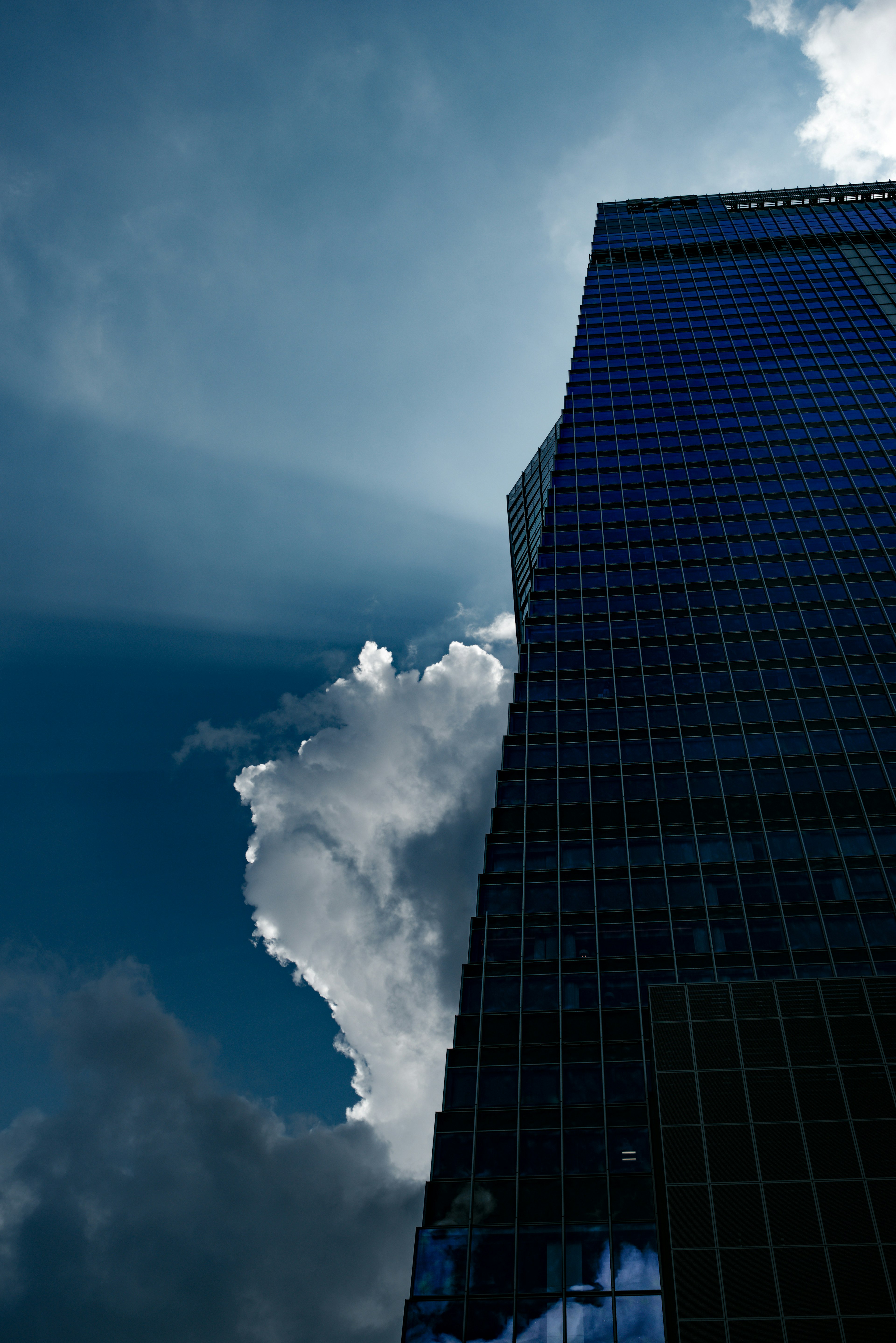 Hohes Gebäude mit blauer Glasfassade vor dramatischen Wolken