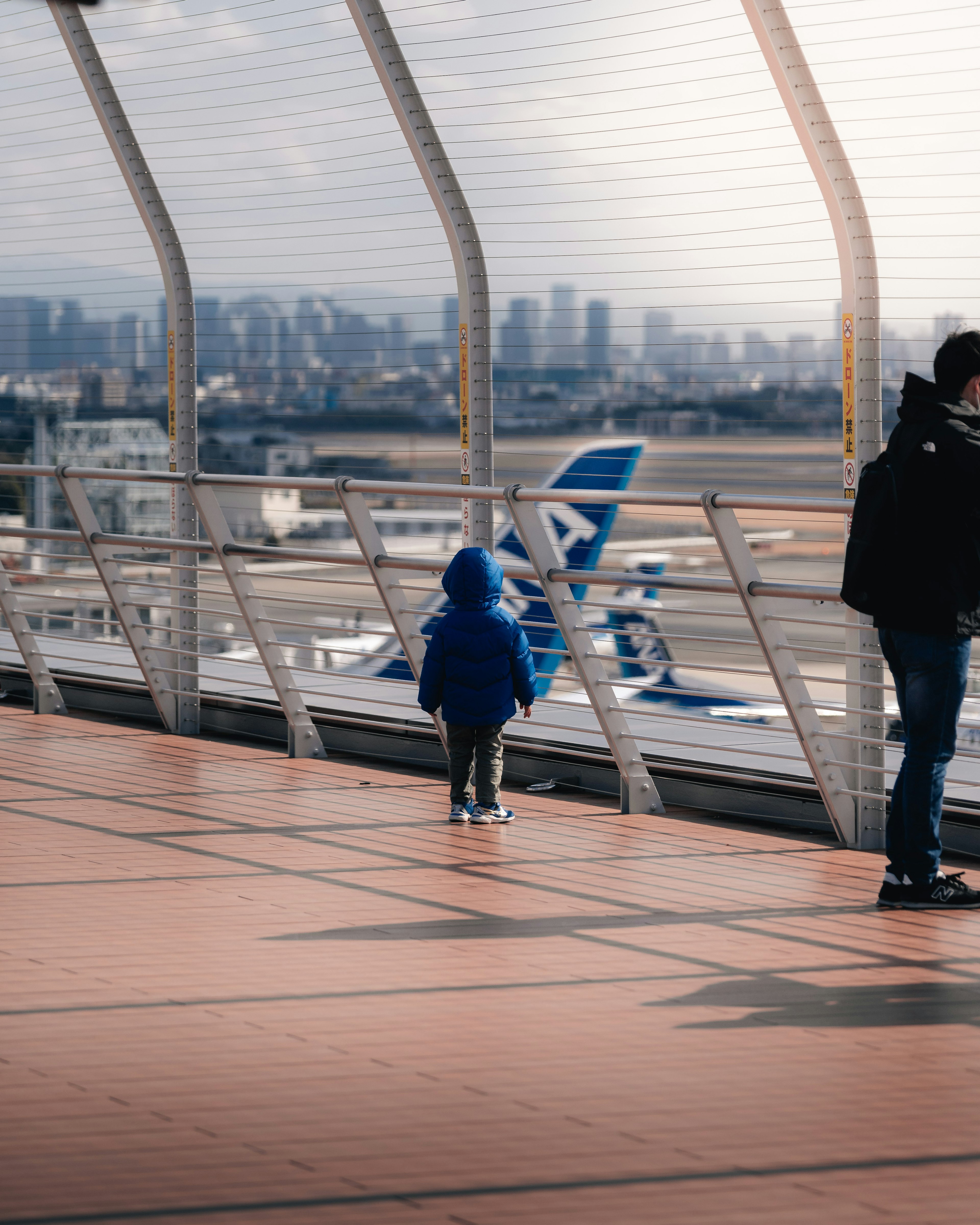 파란 코트를 입은 아이가 도시 스카이라인이 배경인 공항 데크에 서 있는 모습