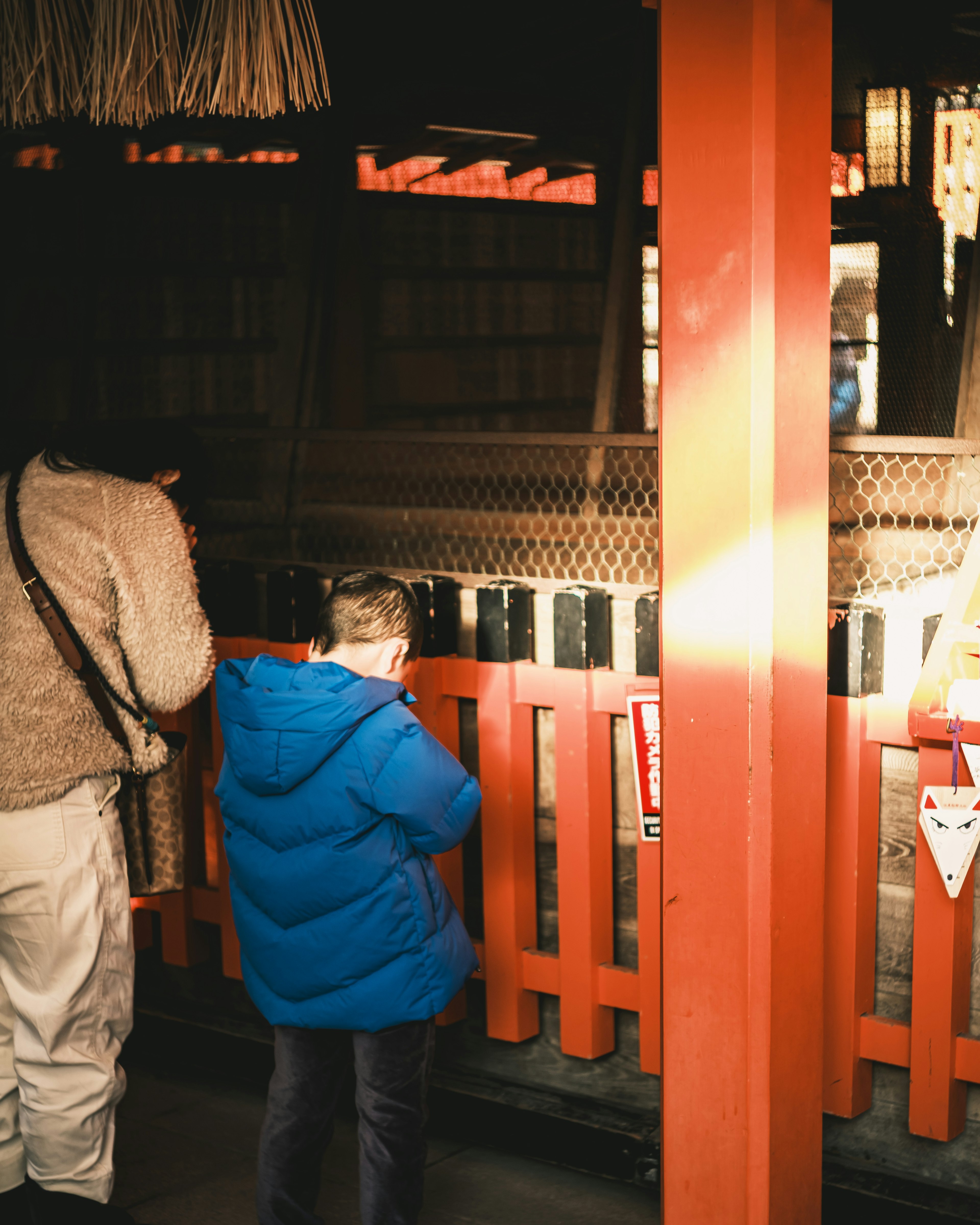 A child in a blue jacket and an adult standing in front of a red fence