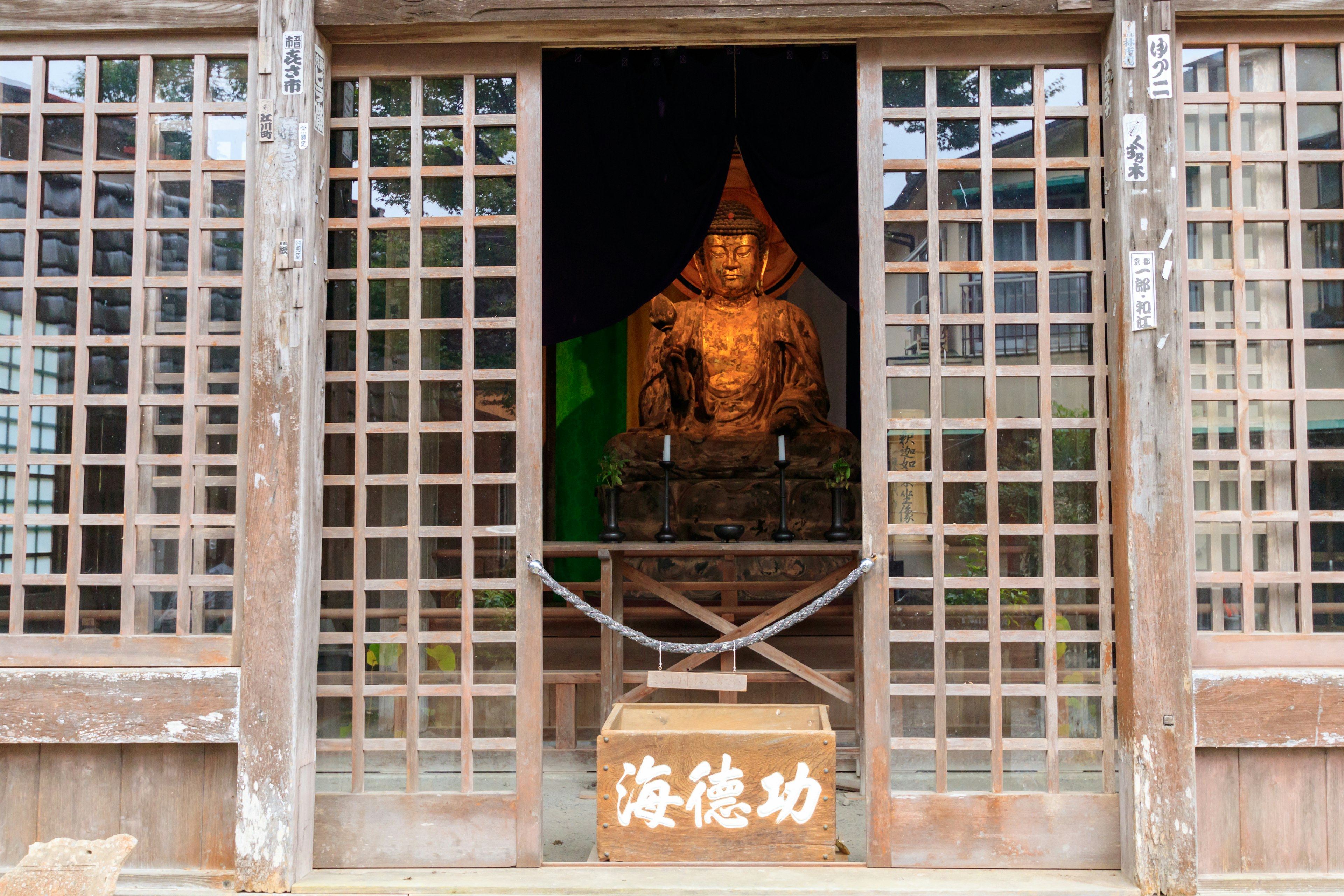 ประตูไม้ลายตาข่ายที่เผยให้เห็นรูปปั้นพระพุทธรูปที่เงียบสงบและบรรยากาศรอบๆ