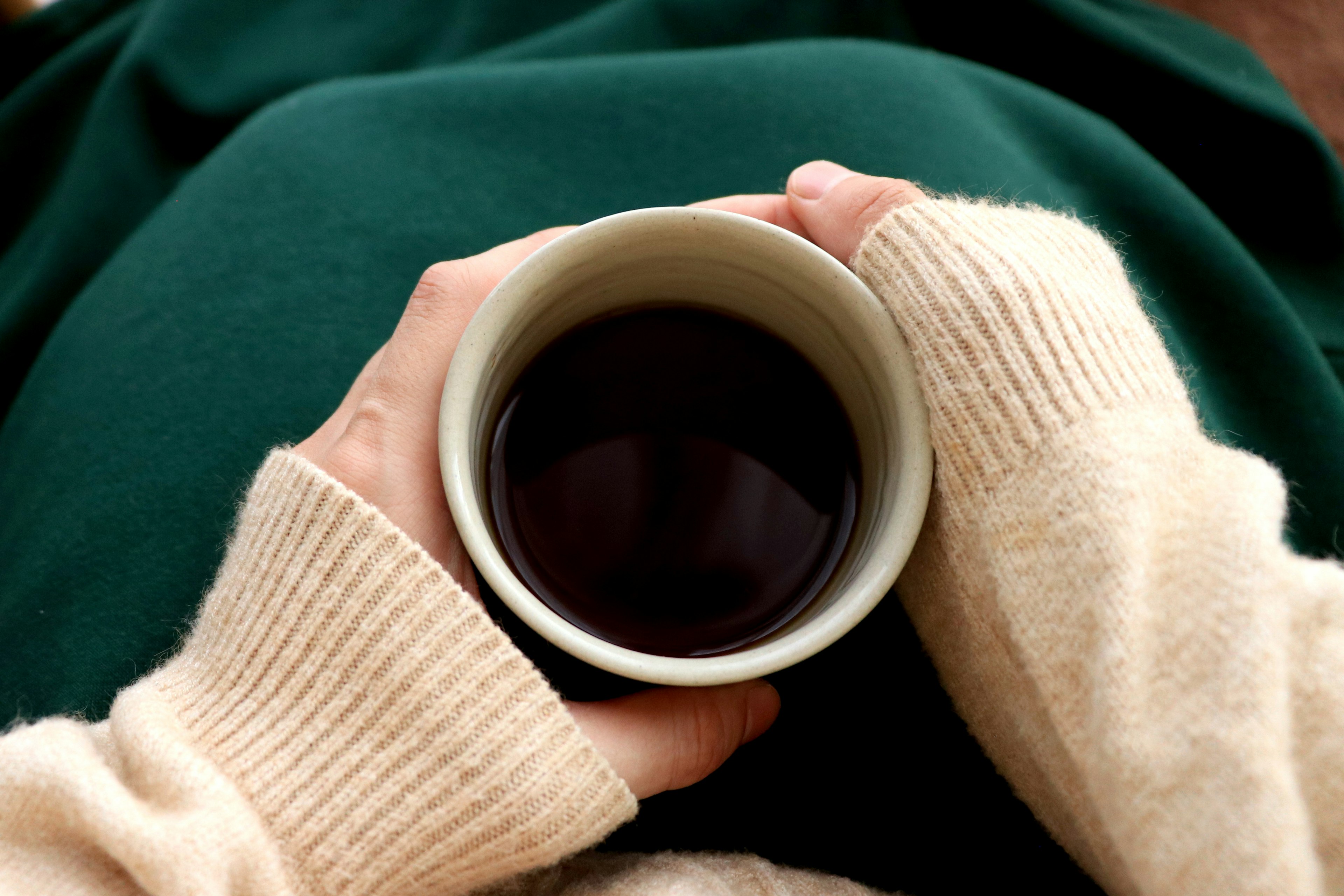 Hands holding a warm drink in a simple cup on a green fabric background