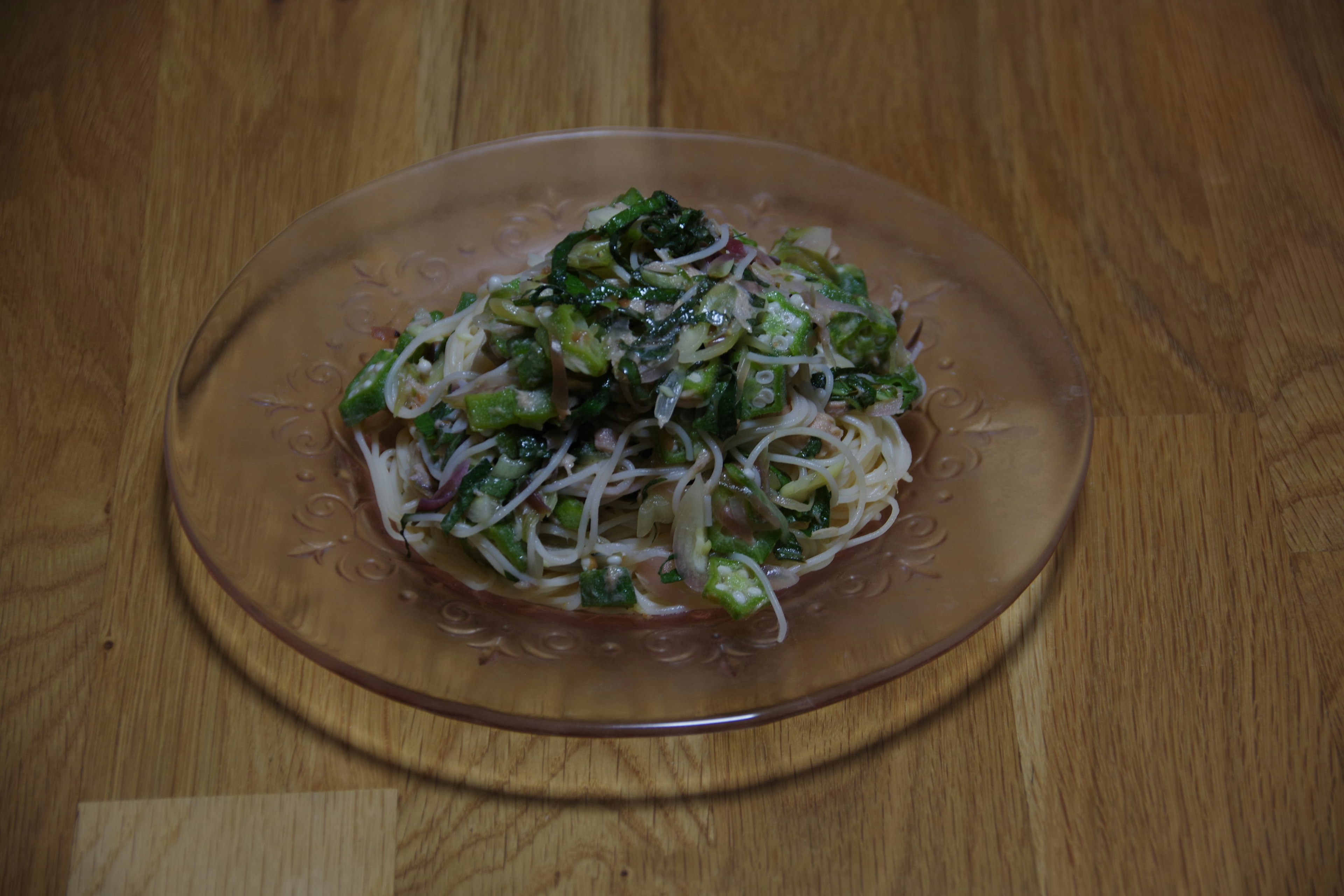 Thin noodles topped with fresh vegetables on a clear plate