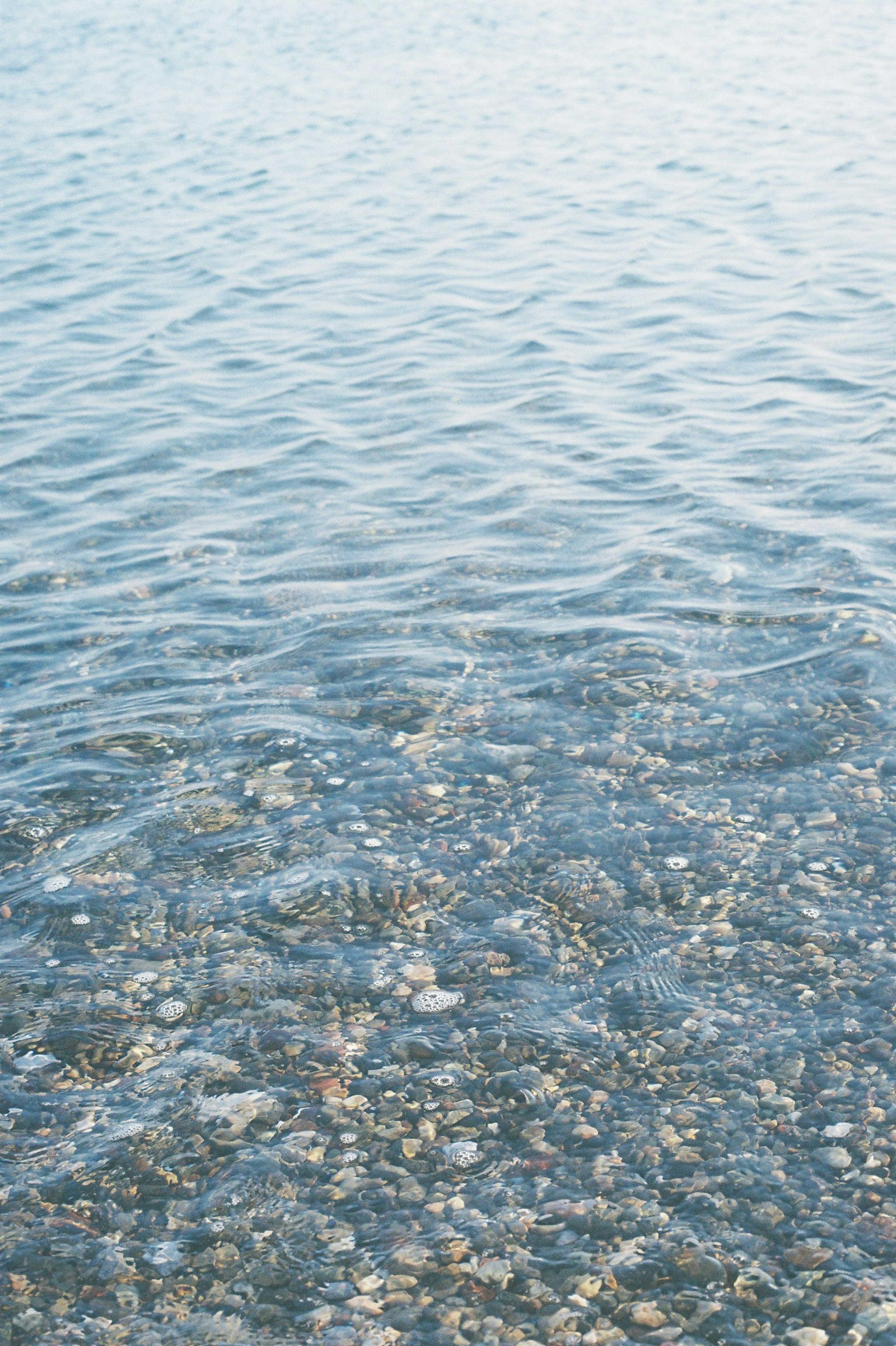 Surface d'eau ondulante avec des galets visibles en dessous