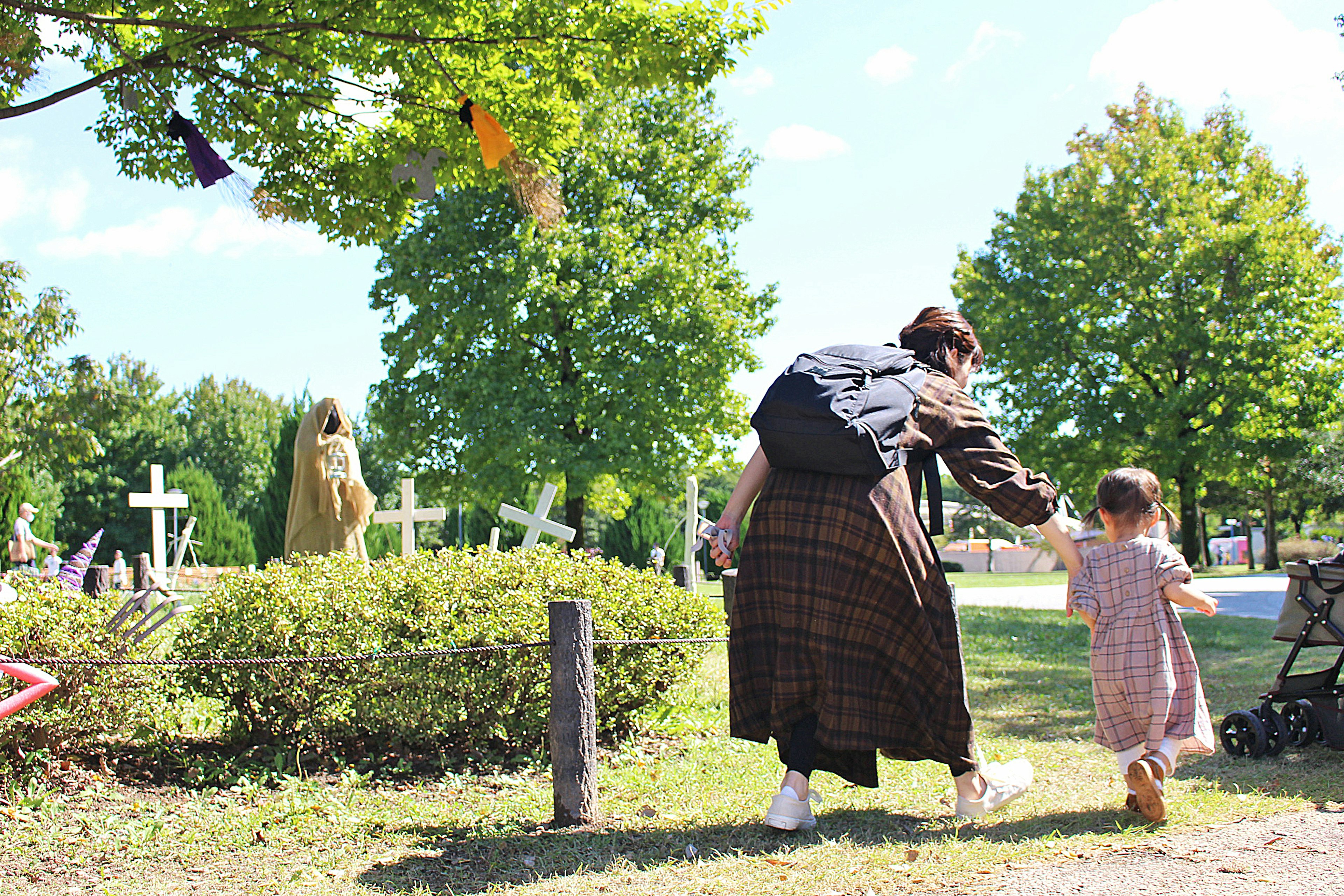 公園で手をつないで歩く大人と子供の後ろ姿 緑の木々と青い空の背景