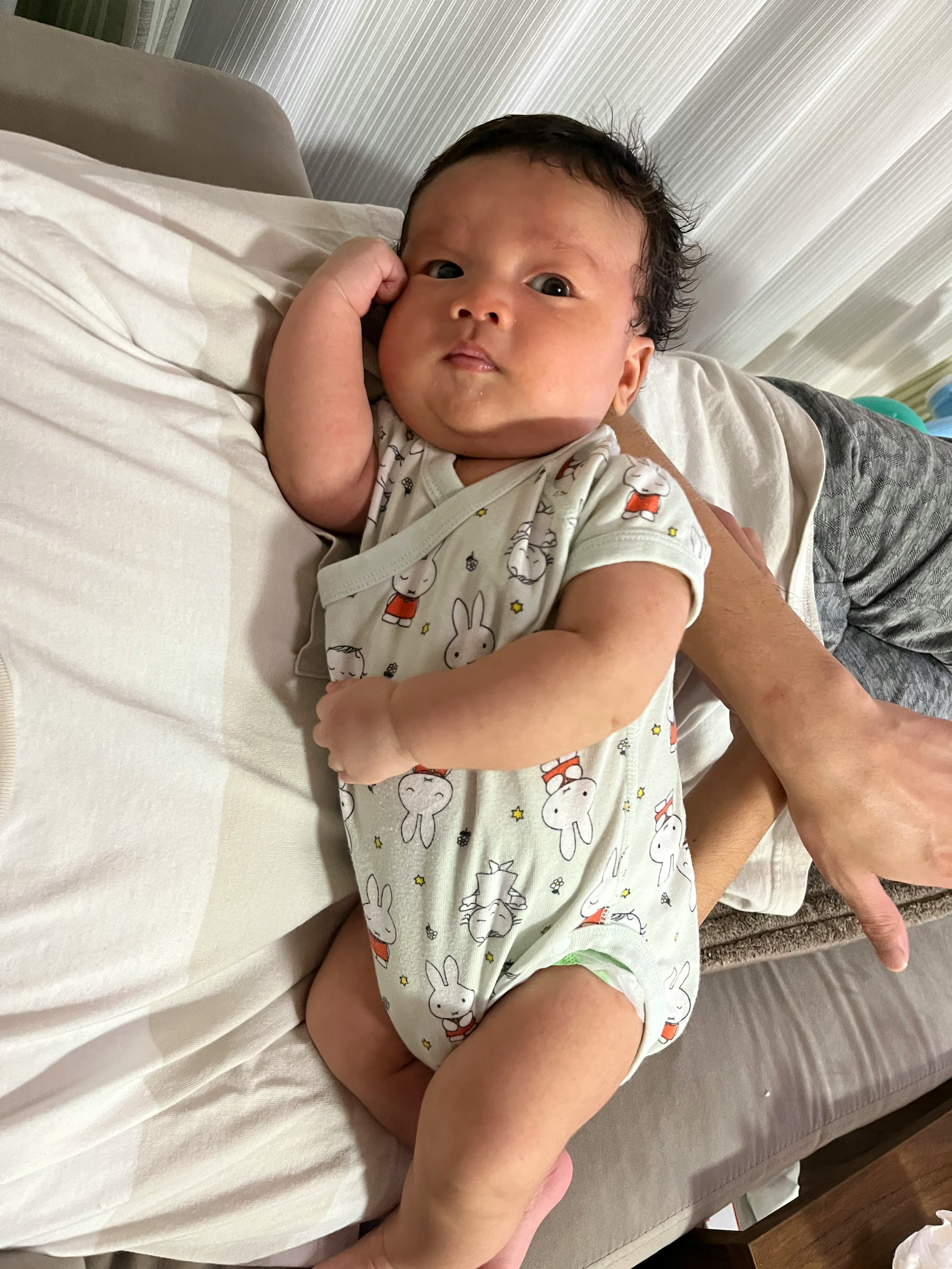 A baby relaxing on a sofa, lying on a white bed sheet