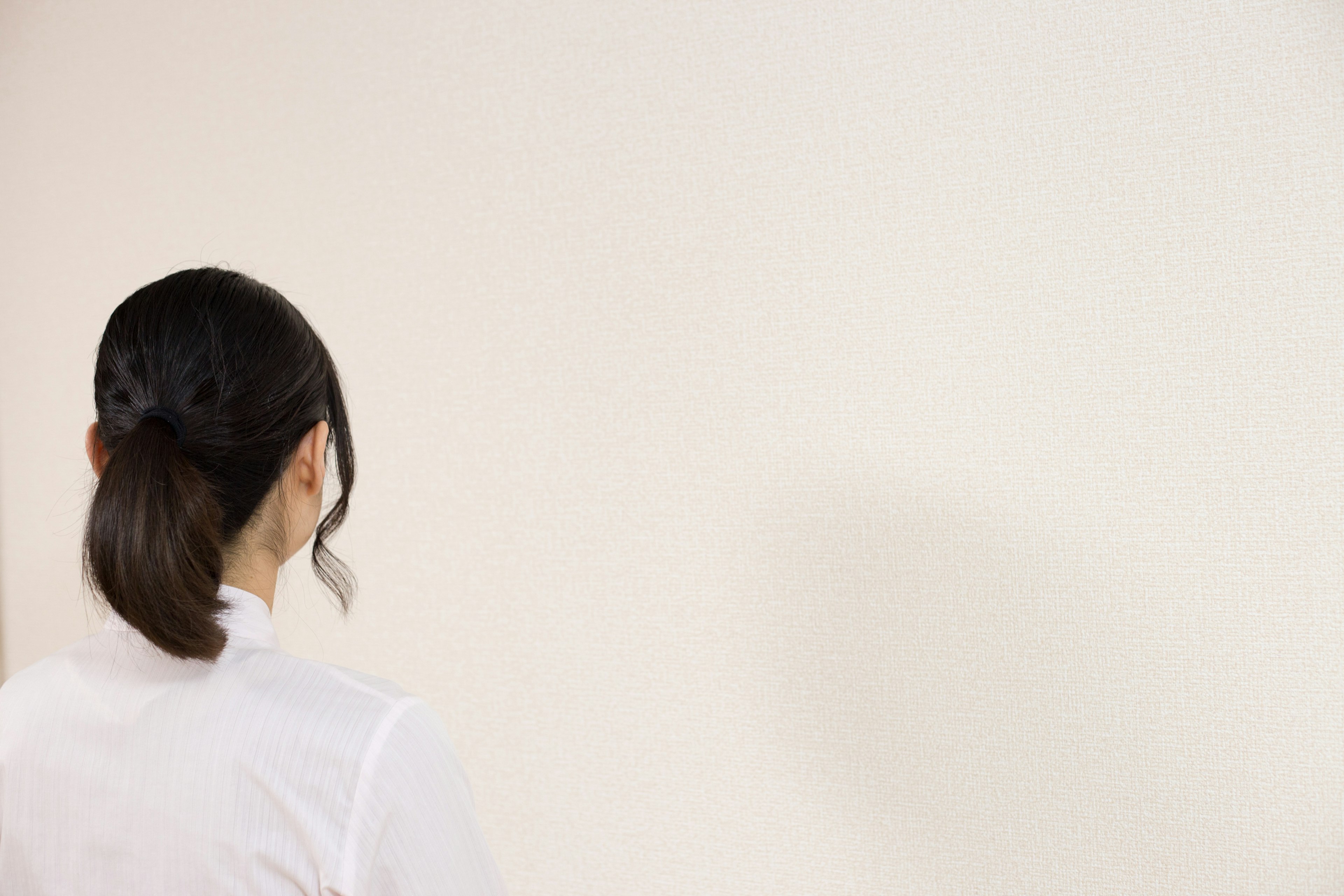 Una donna vista di spalle di fronte a un muro bianco semplice