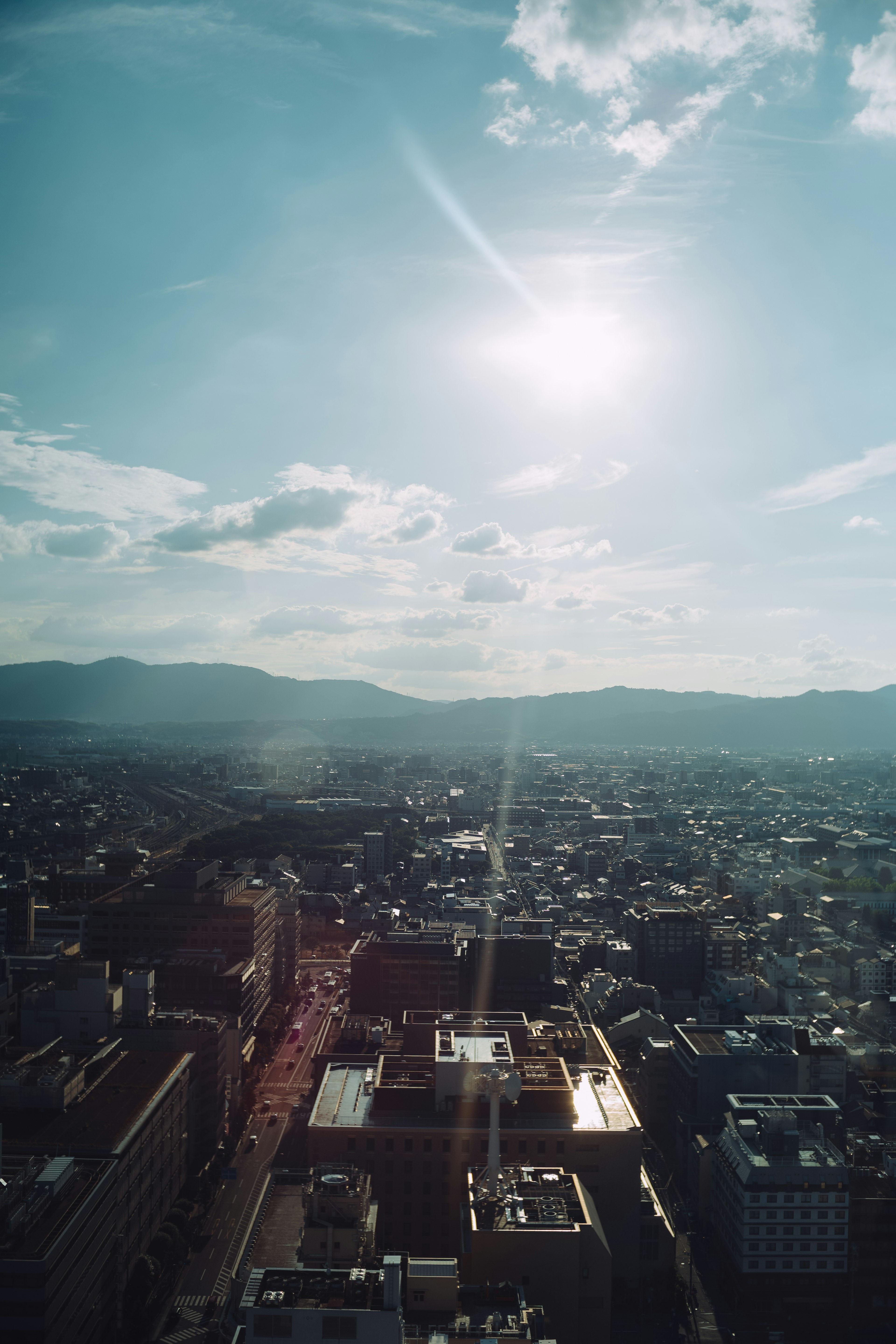 Vista de la ciudad bajo un cielo azul con sol montañas al fondo