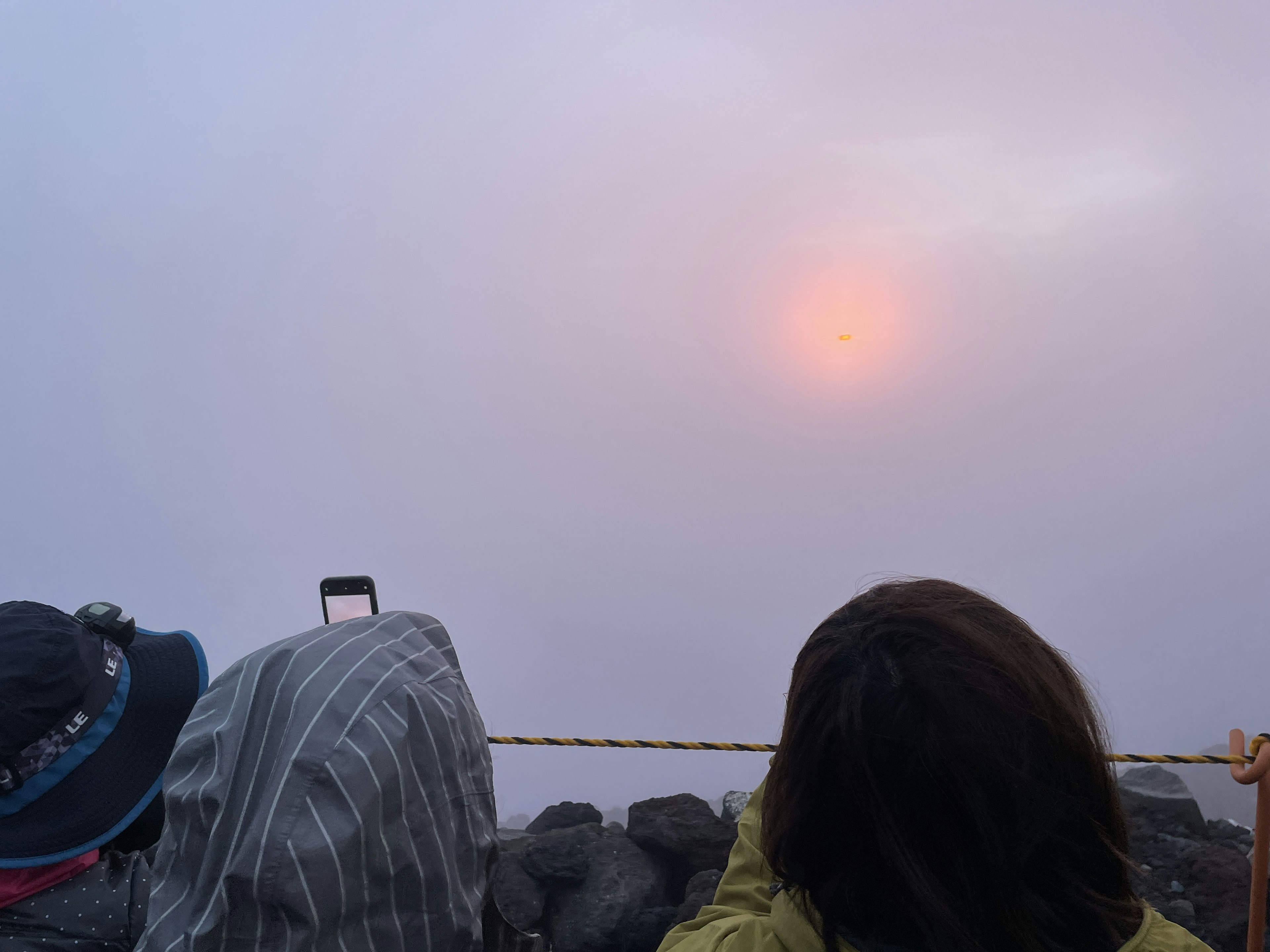 霧の中から現れる夕日を見つめる人々