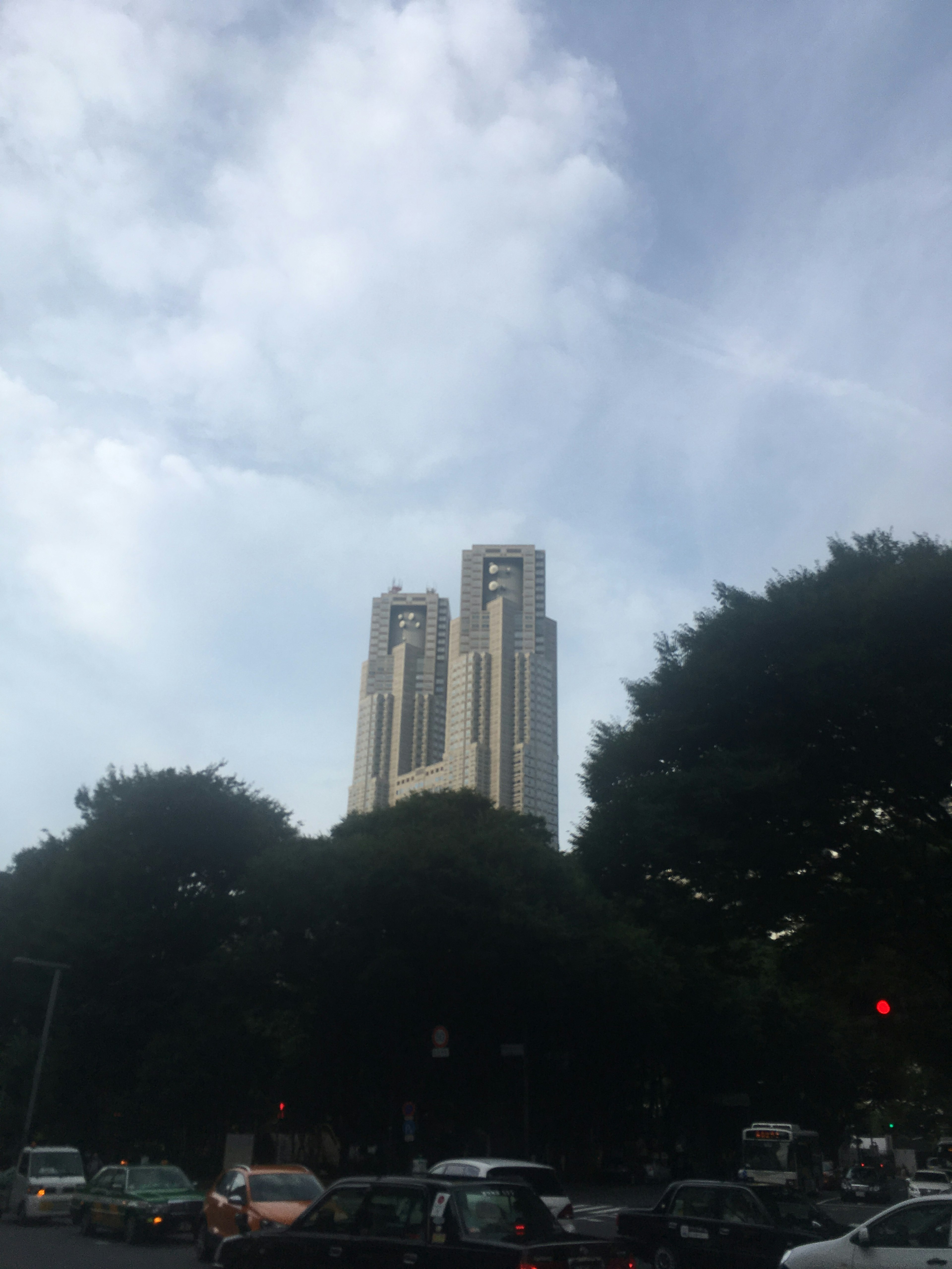 A skyscraper partially obscured by trees with a cloudy sky