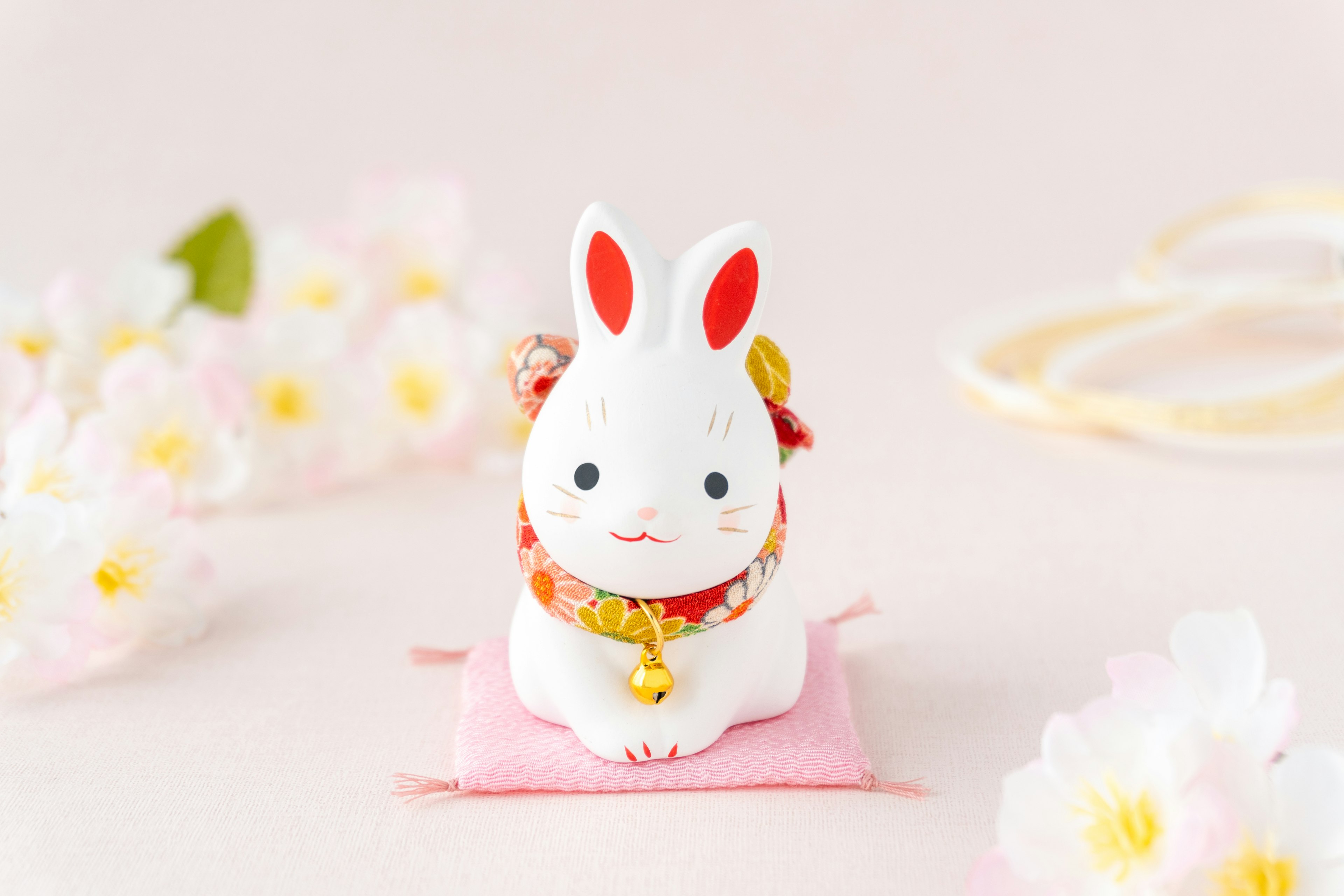 A cute rabbit figurine sitting on a pink cushion surrounded by cherry blossom flowers