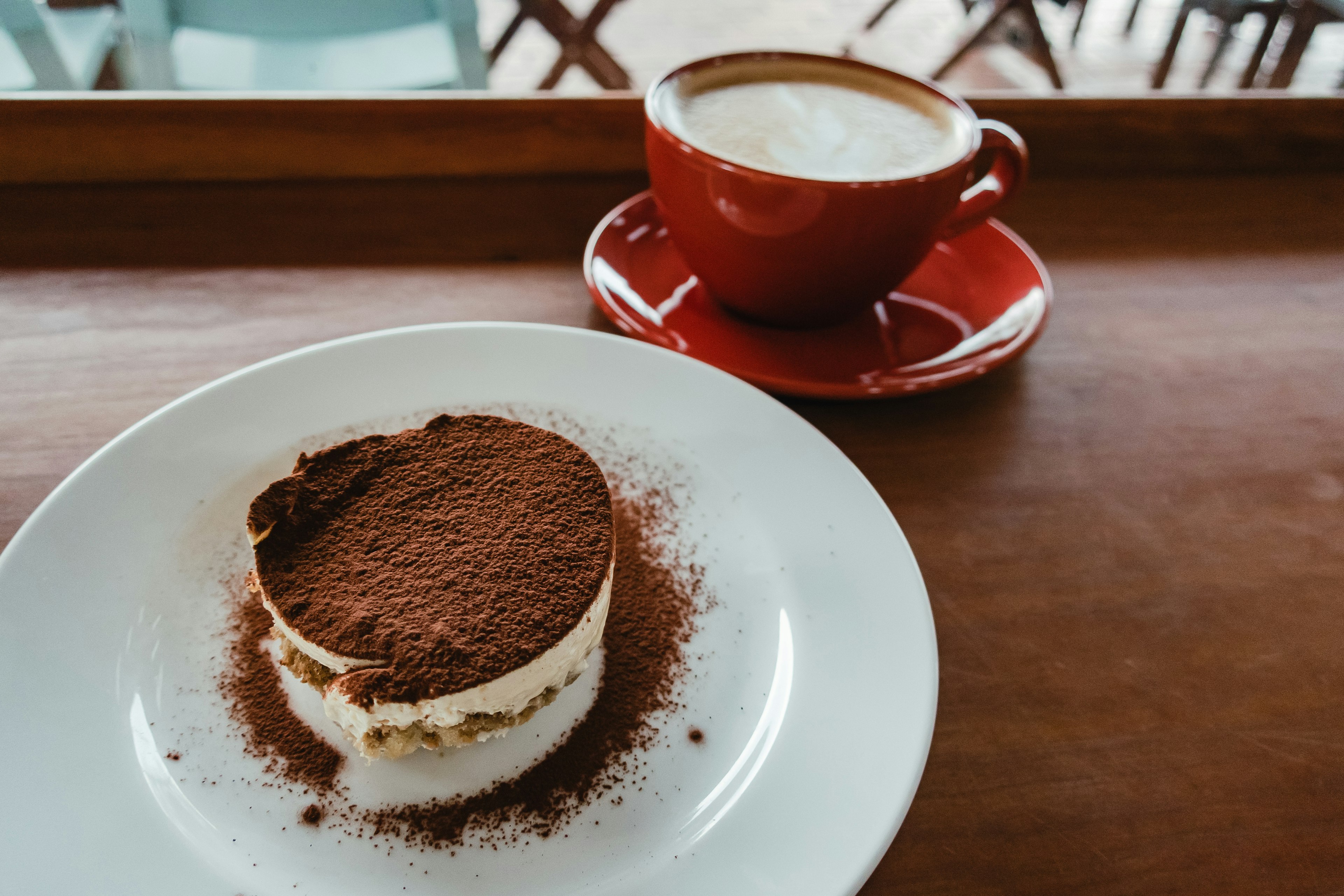 Tiramisu dengan taburan cokelat disajikan dengan secangkir cappuccino