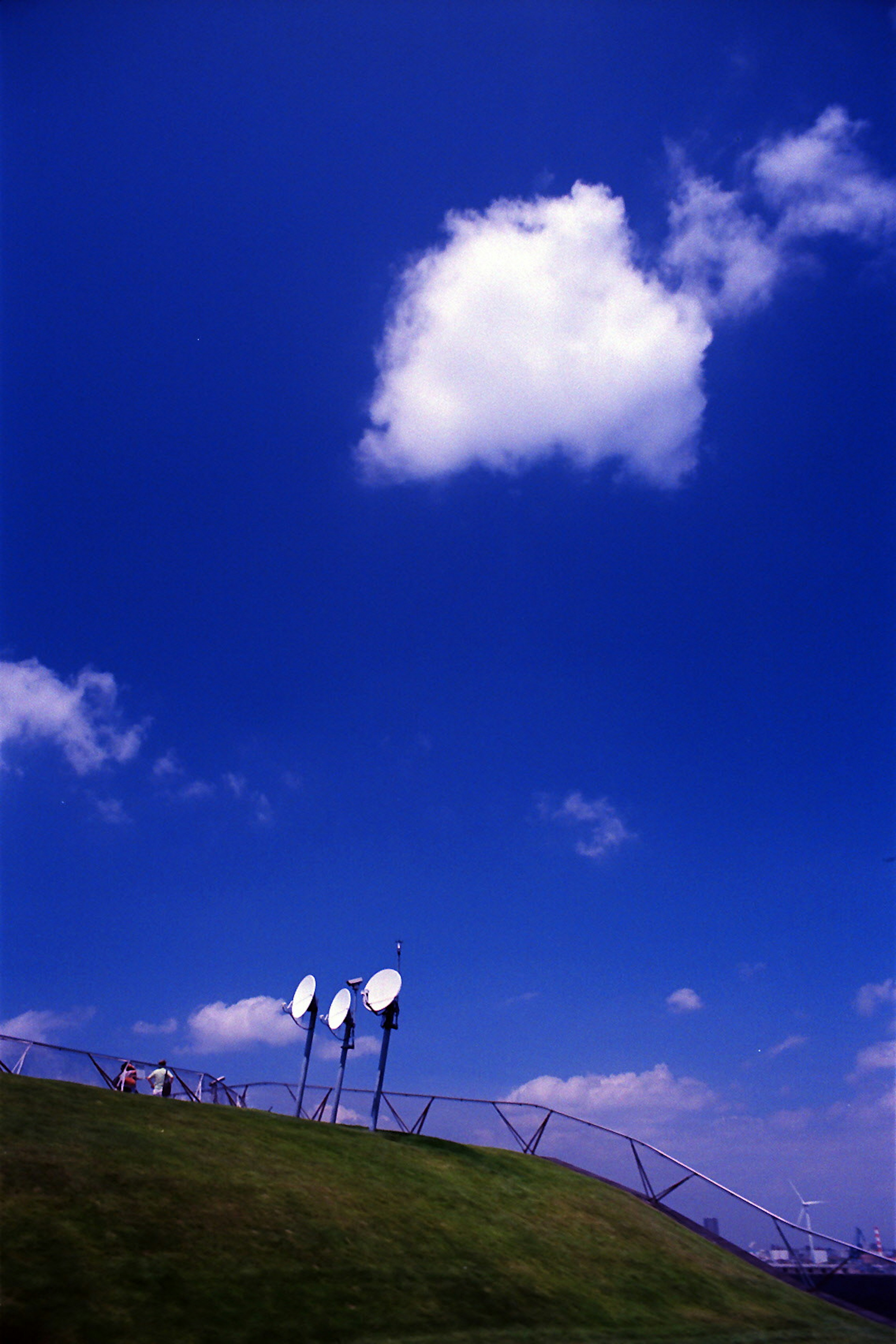 Drei Satellitenantennen auf einem grünen Hügel unter einem klaren blauen Himmel