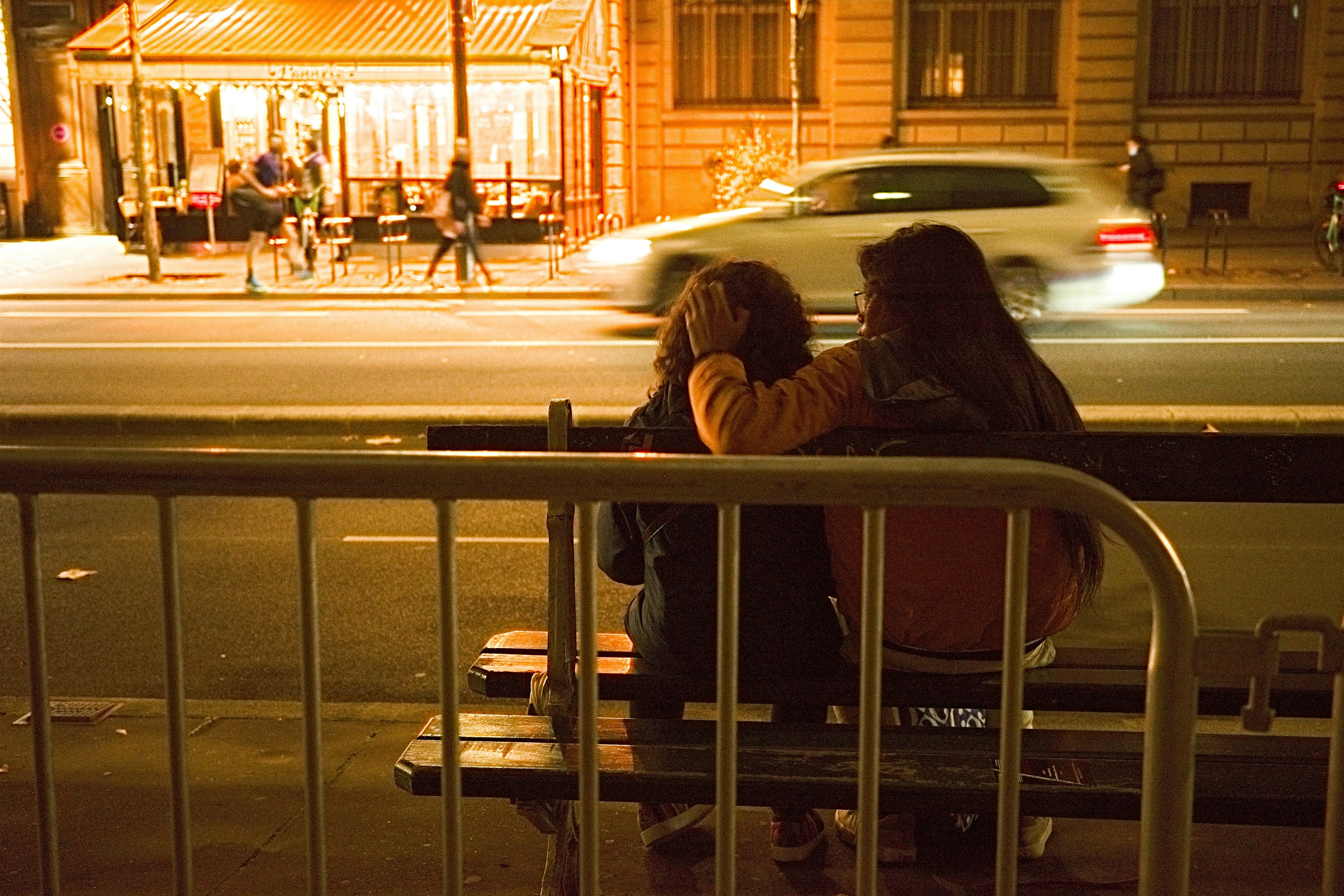 夜の街でベンチに座る二人の女性が親しそうにしている